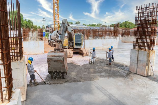 Construction workers pouring concrete at a building site with a backhoe and steel rebar columns