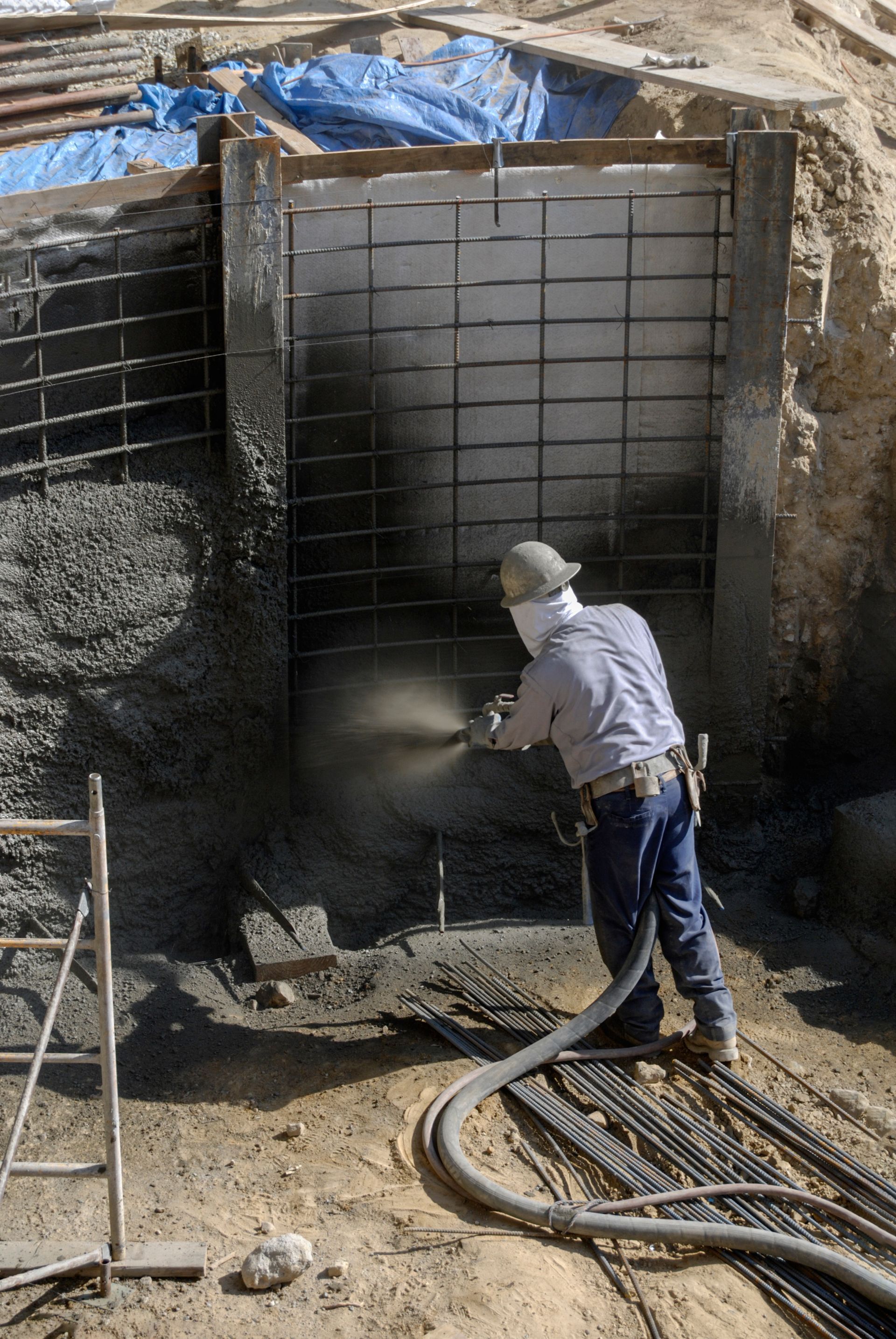 Worker spraying concrete inside a deep excavation with rebar walls and hoses attached Worker spraying concrete inside a deep excavation with rebar walls and hoses attached