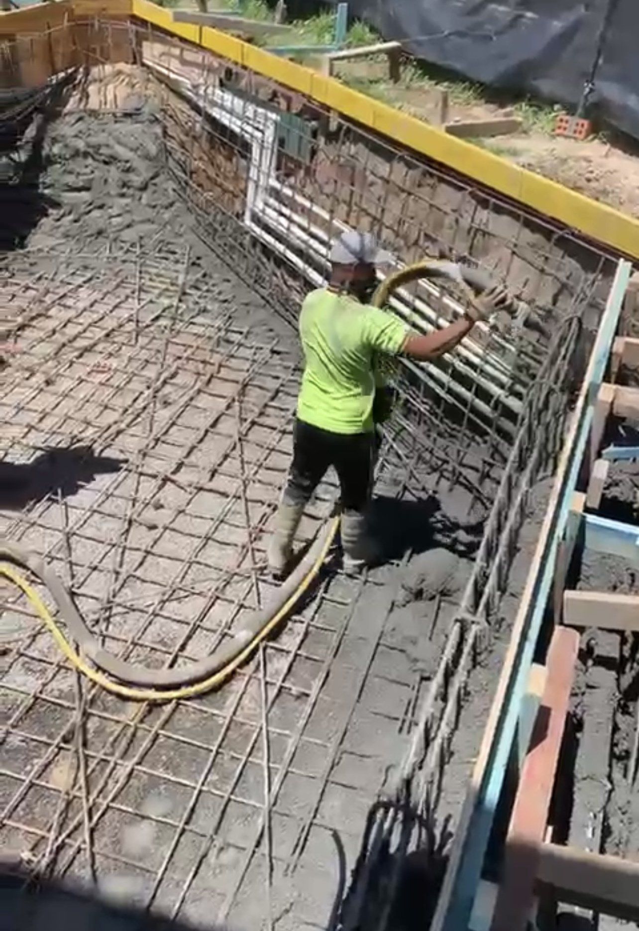 Worker in neon green shirt spraying concrete onto reinforced foundation walls.