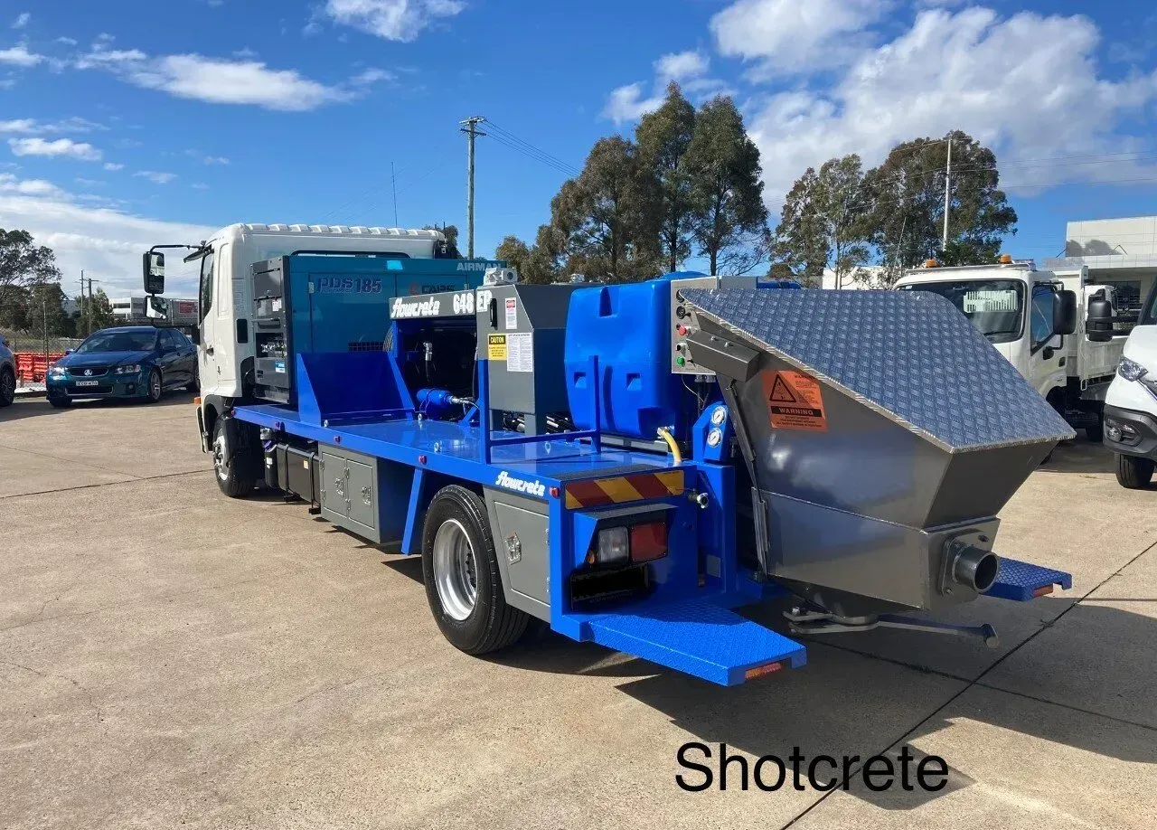 Blue shotcrete truck with metal hopper parked outdoors on a sunny day
