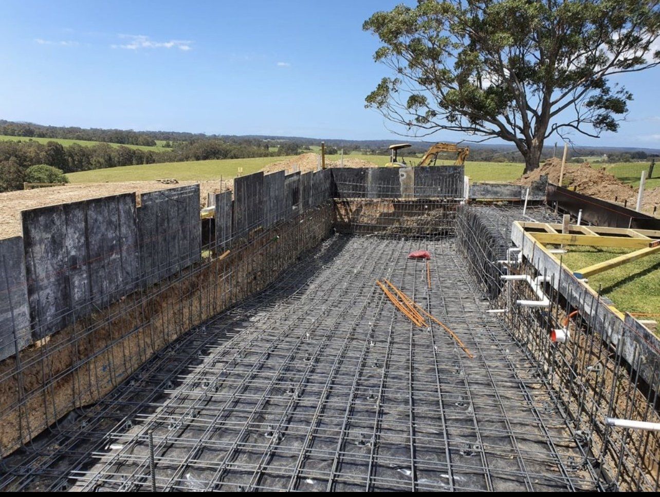 Concrete foundation under construction with rebar grid, retaining walls, and a tree in the background