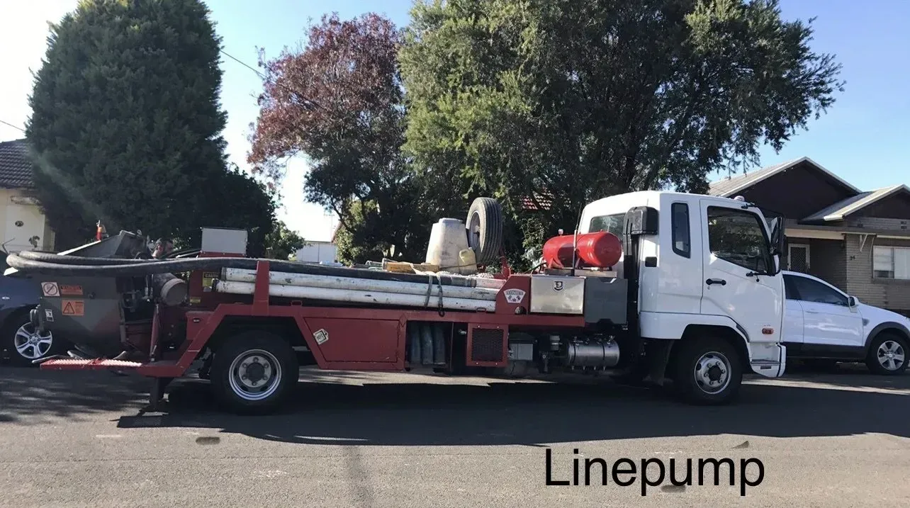 Red-and-white line pump truck parked on a residential street with houses and trees behind it.