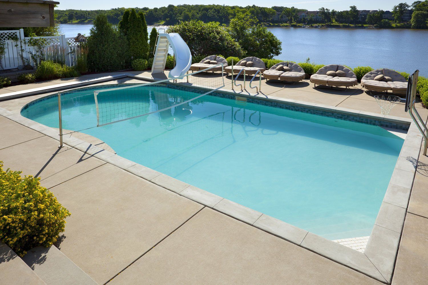 Outdoor swimming pool beside a lake, with lounge chairs, umbrellas, and a sailboat sculpture nearby.
