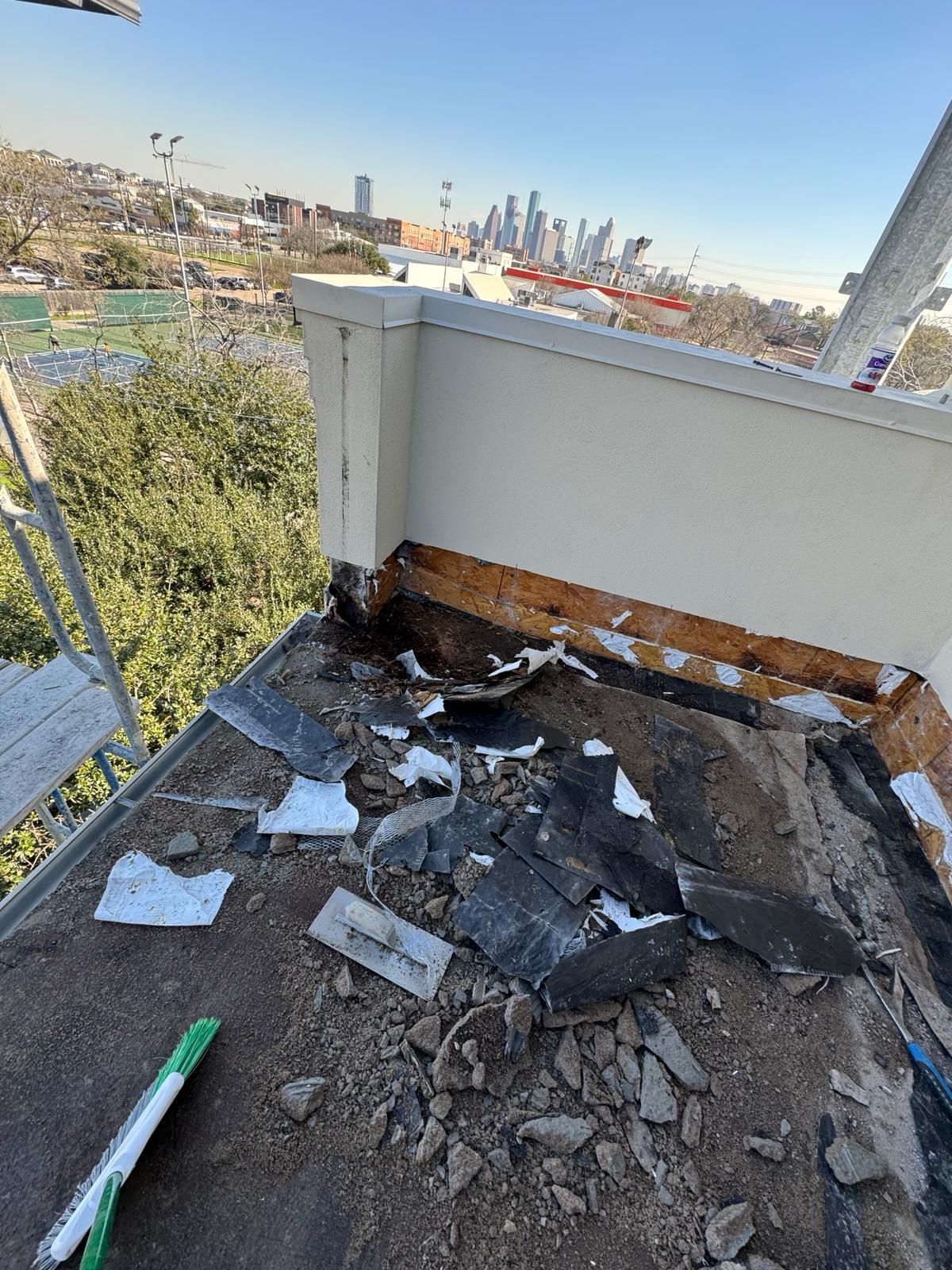 A roof is being repaired on a balcony with a city skyline in the background.