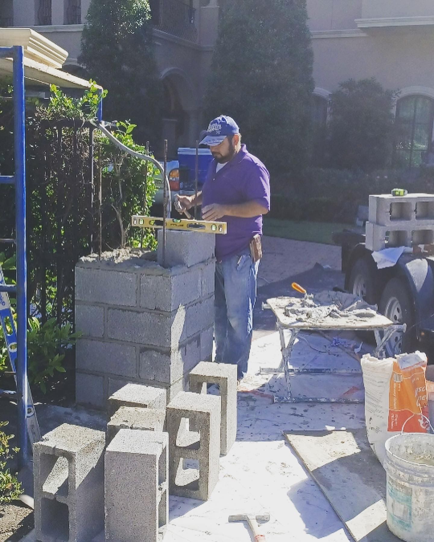 A man in a purple shirt is working on a brick wall