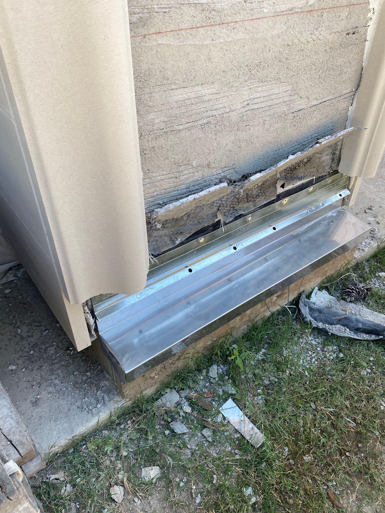 A stainless steel door sill is sitting on the ground next to a concrete wall.