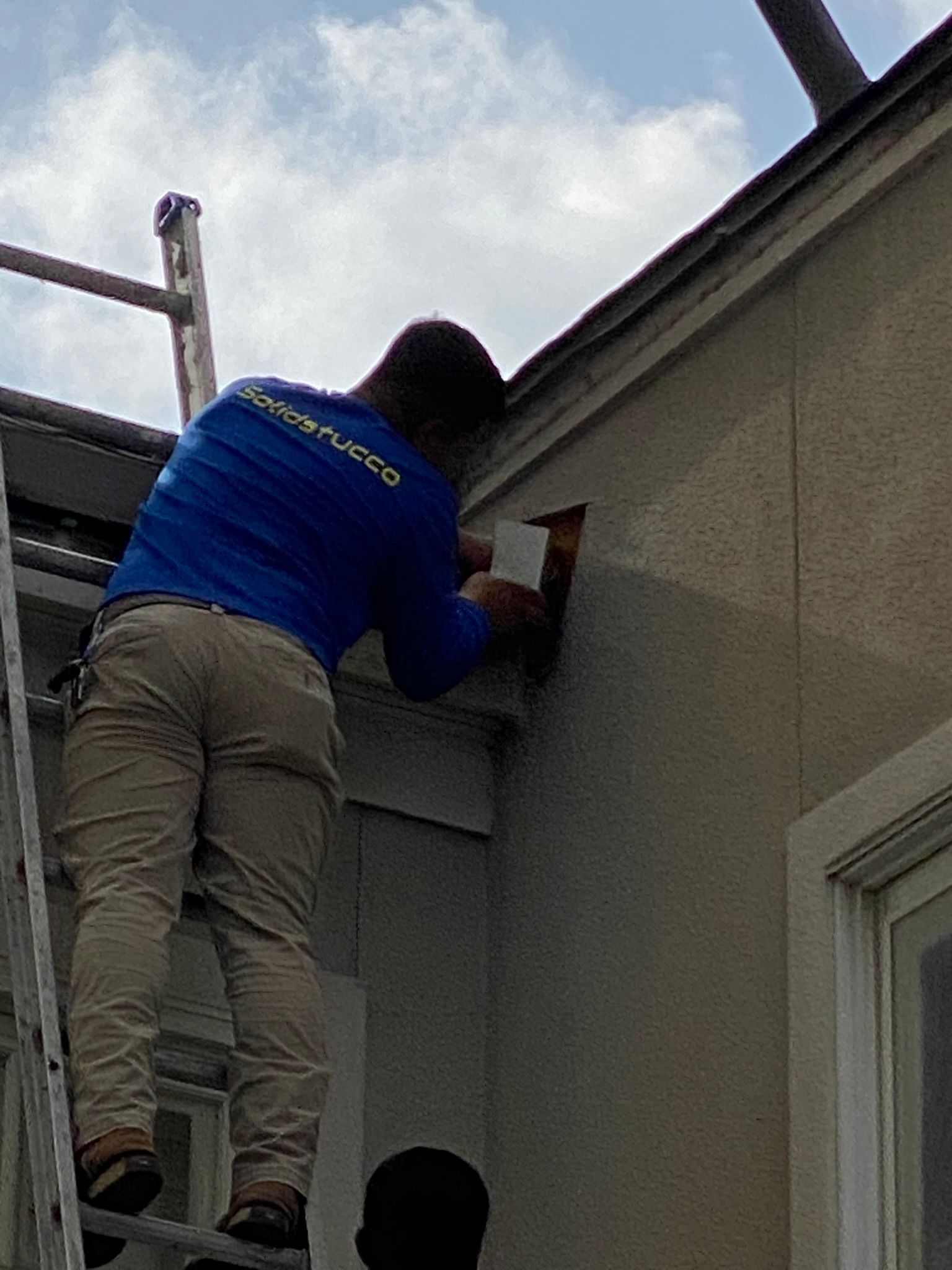 A man is standing on a ladder on the side of a building.