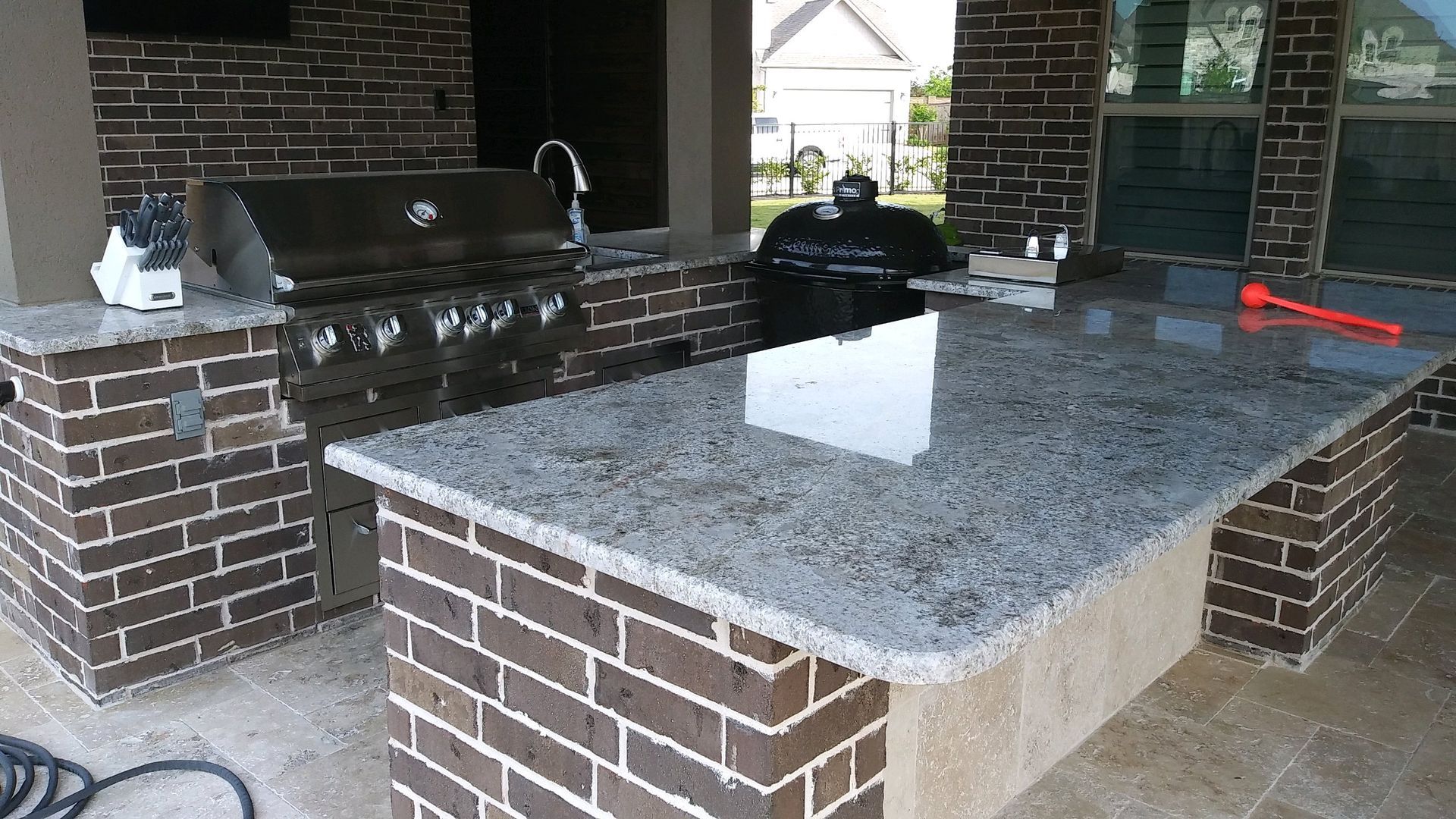 A brick kitchen with a granite counter top and a grill.