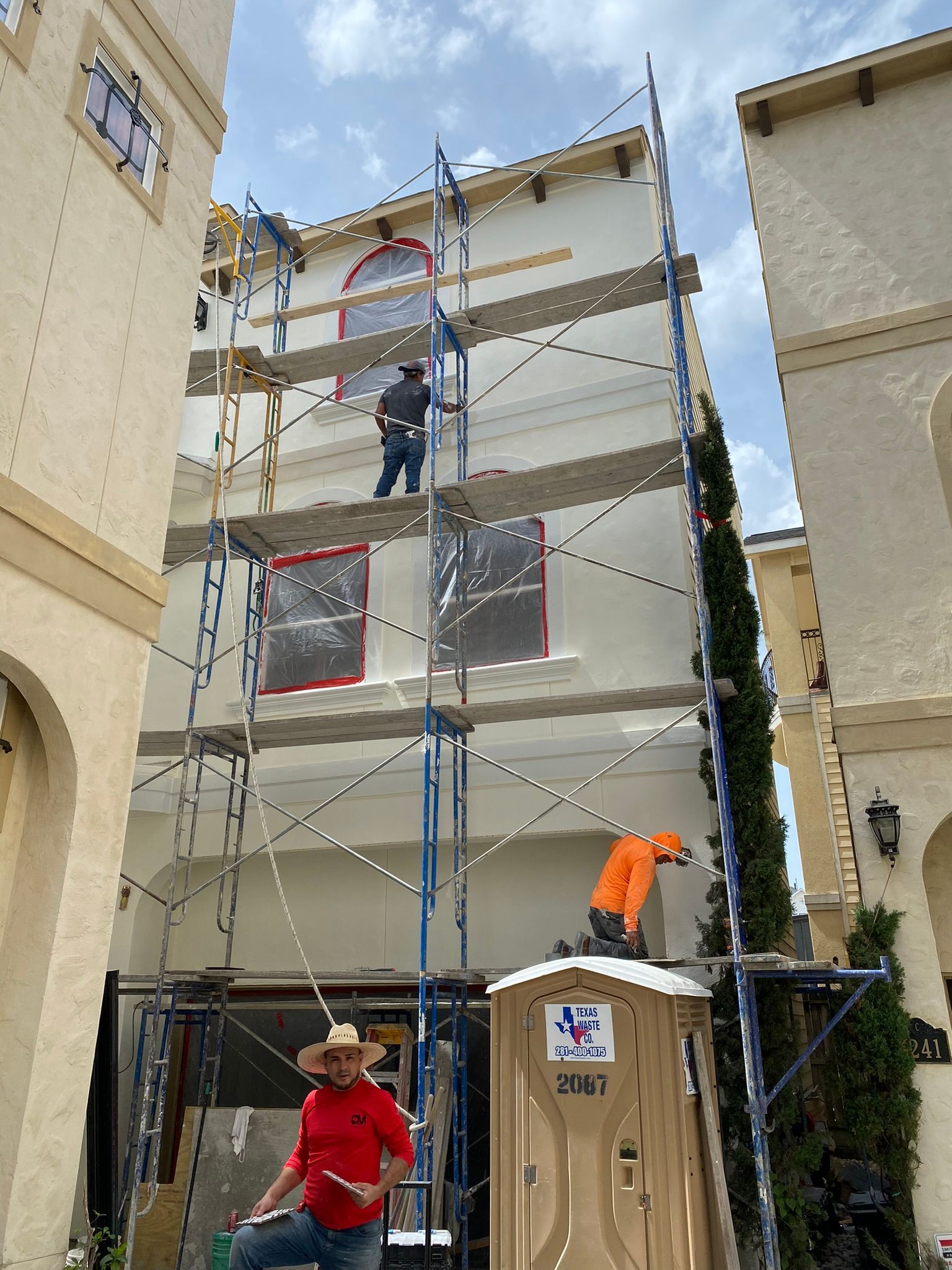 A man in a red shirt is standing in front of a building being painted.