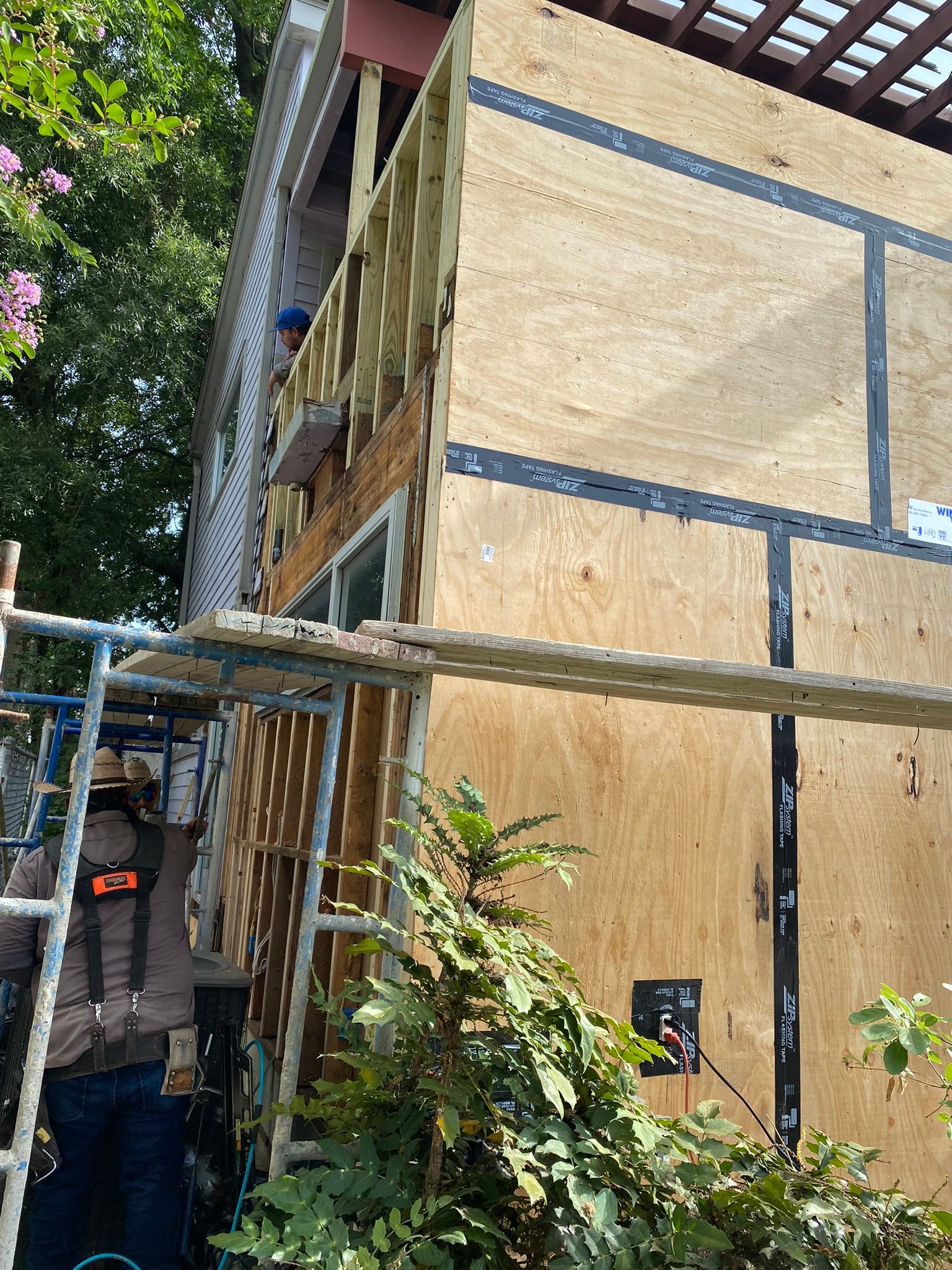 A man is standing on a ladder in front of a house that is being remodeled.