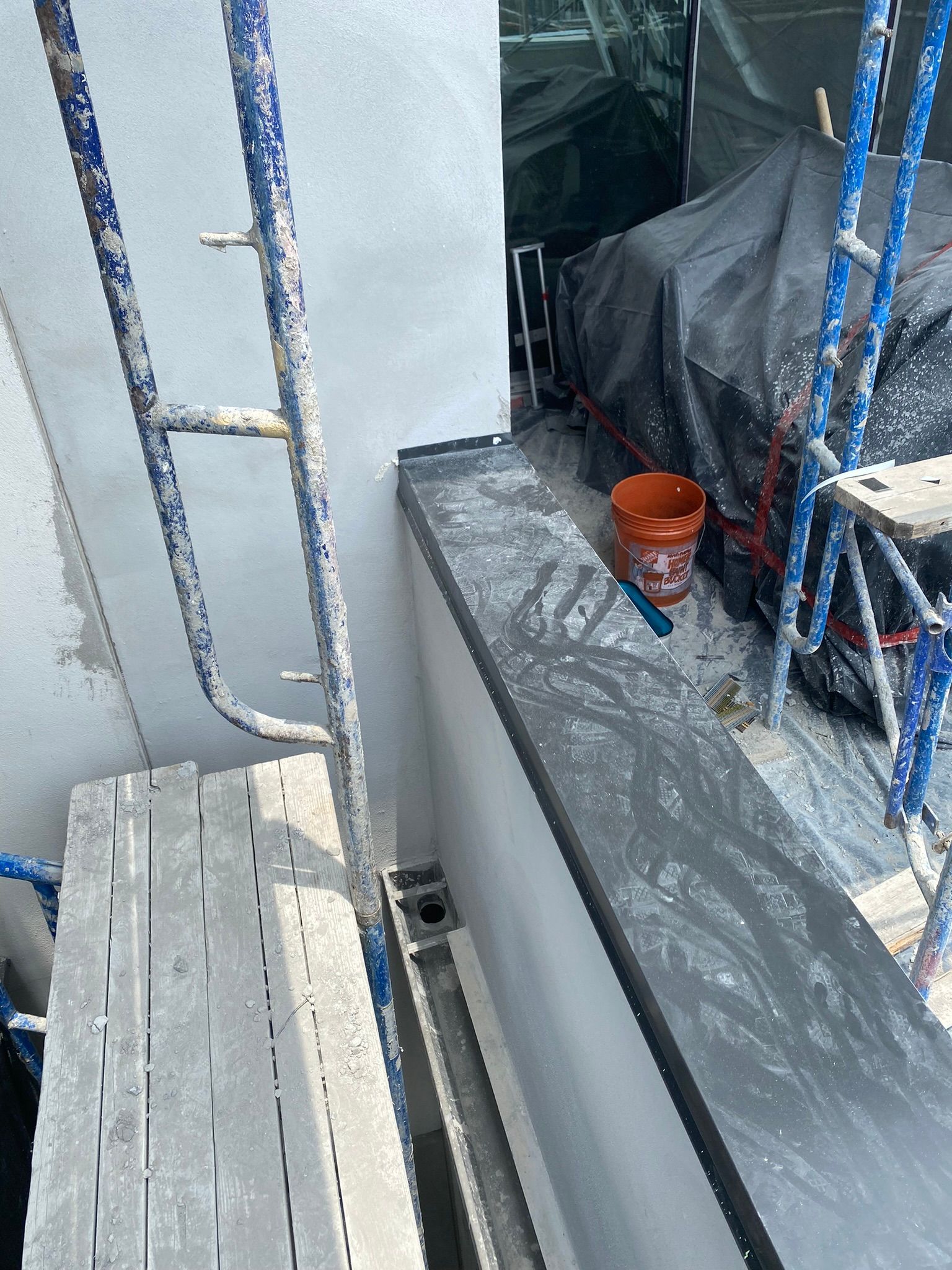 A bucket of paint is sitting on a window sill next to a ladder.