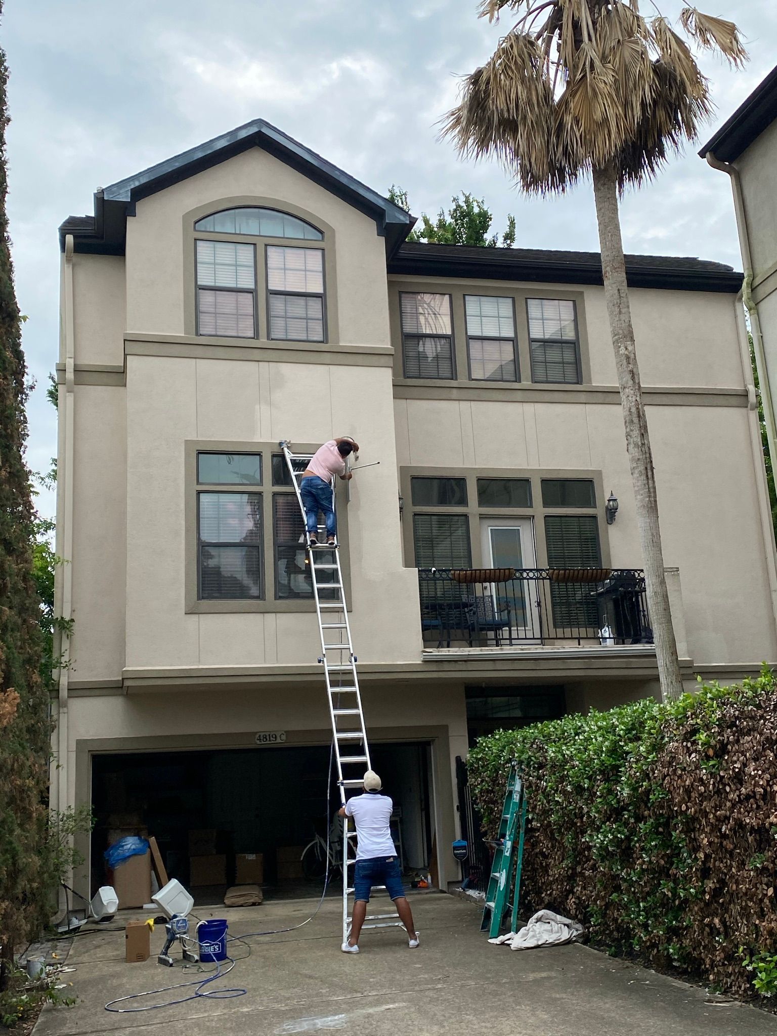 A man on a ladder is painting the side of a house