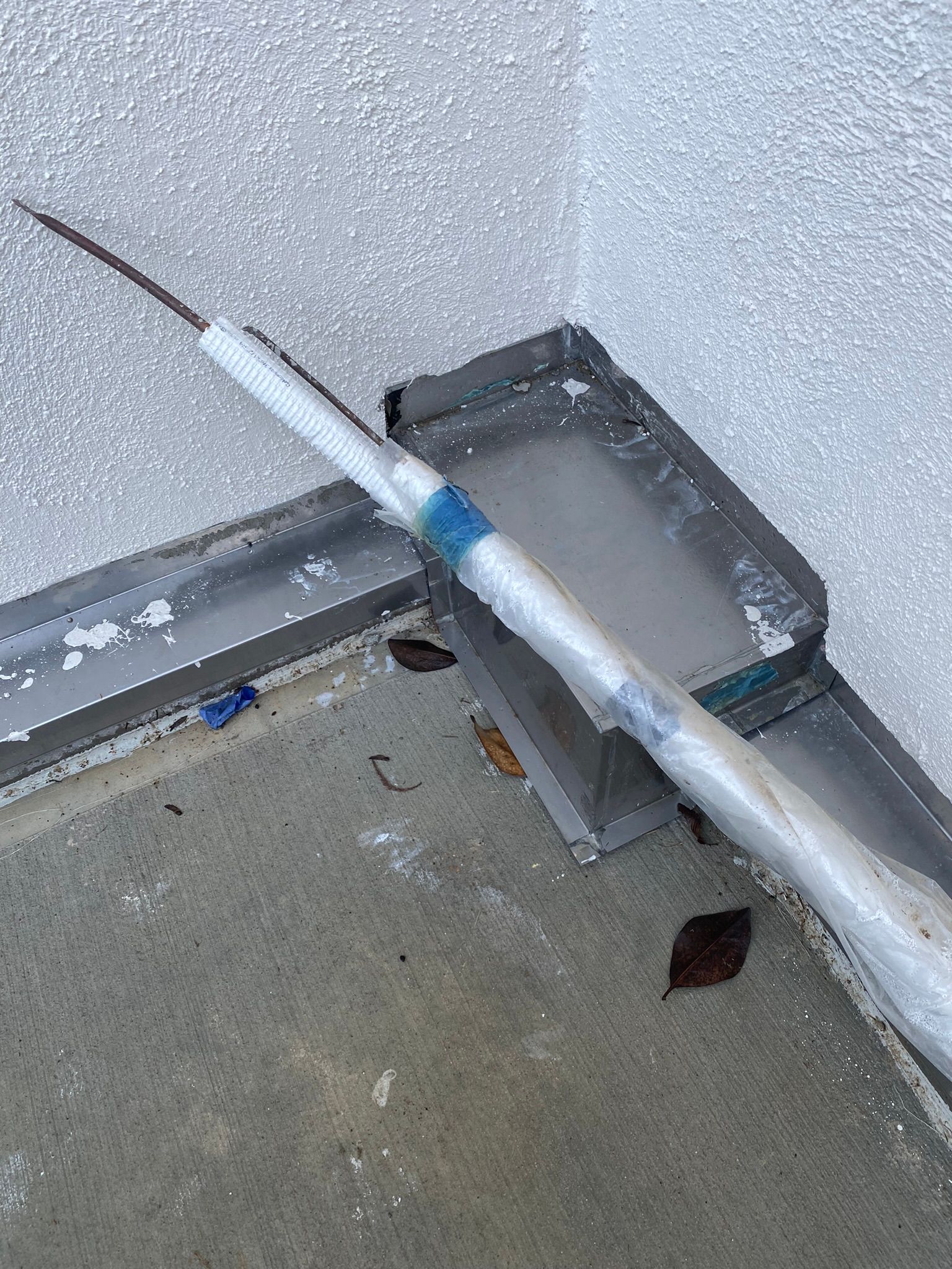 A syringe is sitting on the ground next to a pipe.