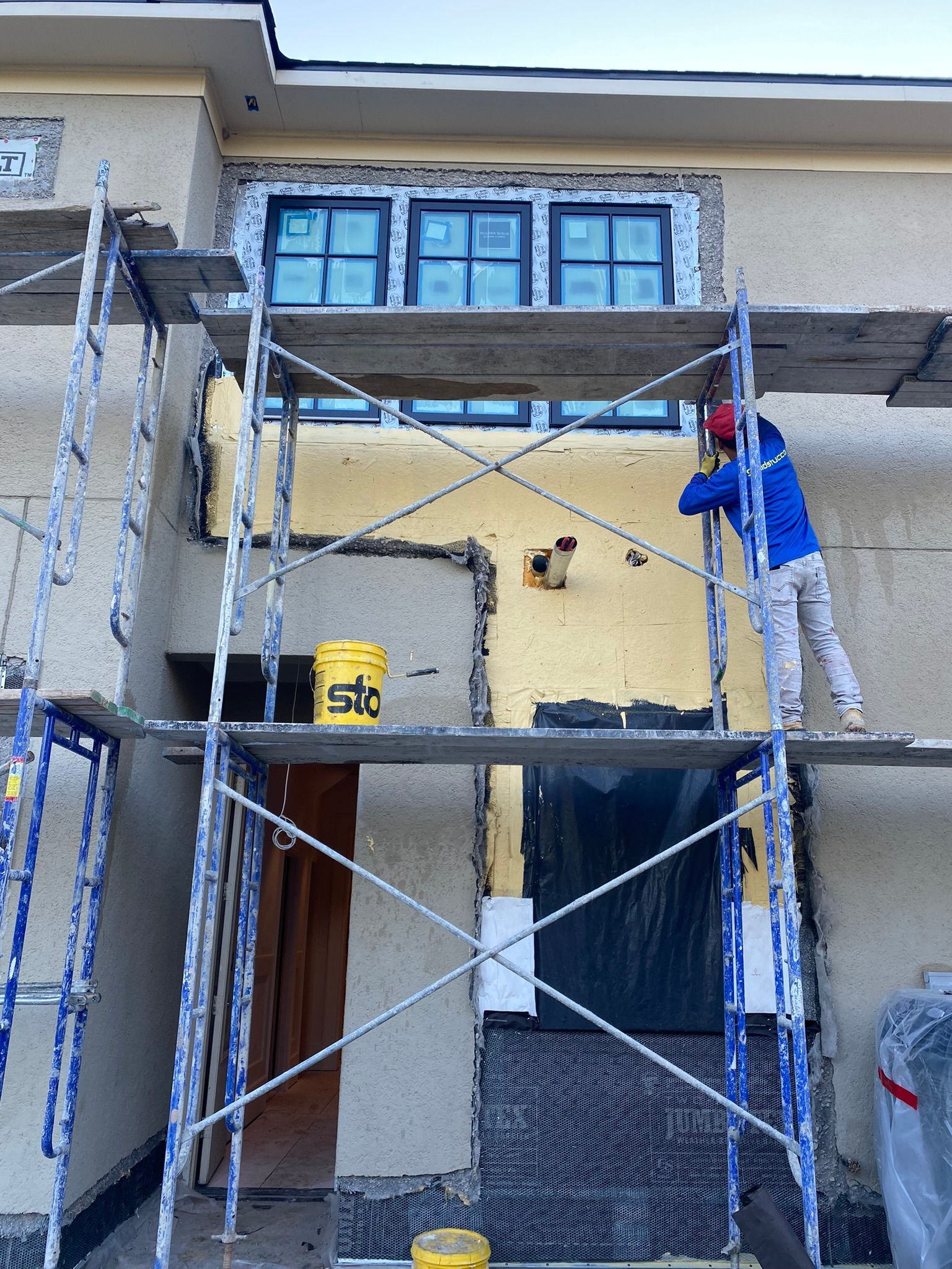 A man is painting the side of a house with scaffolding.