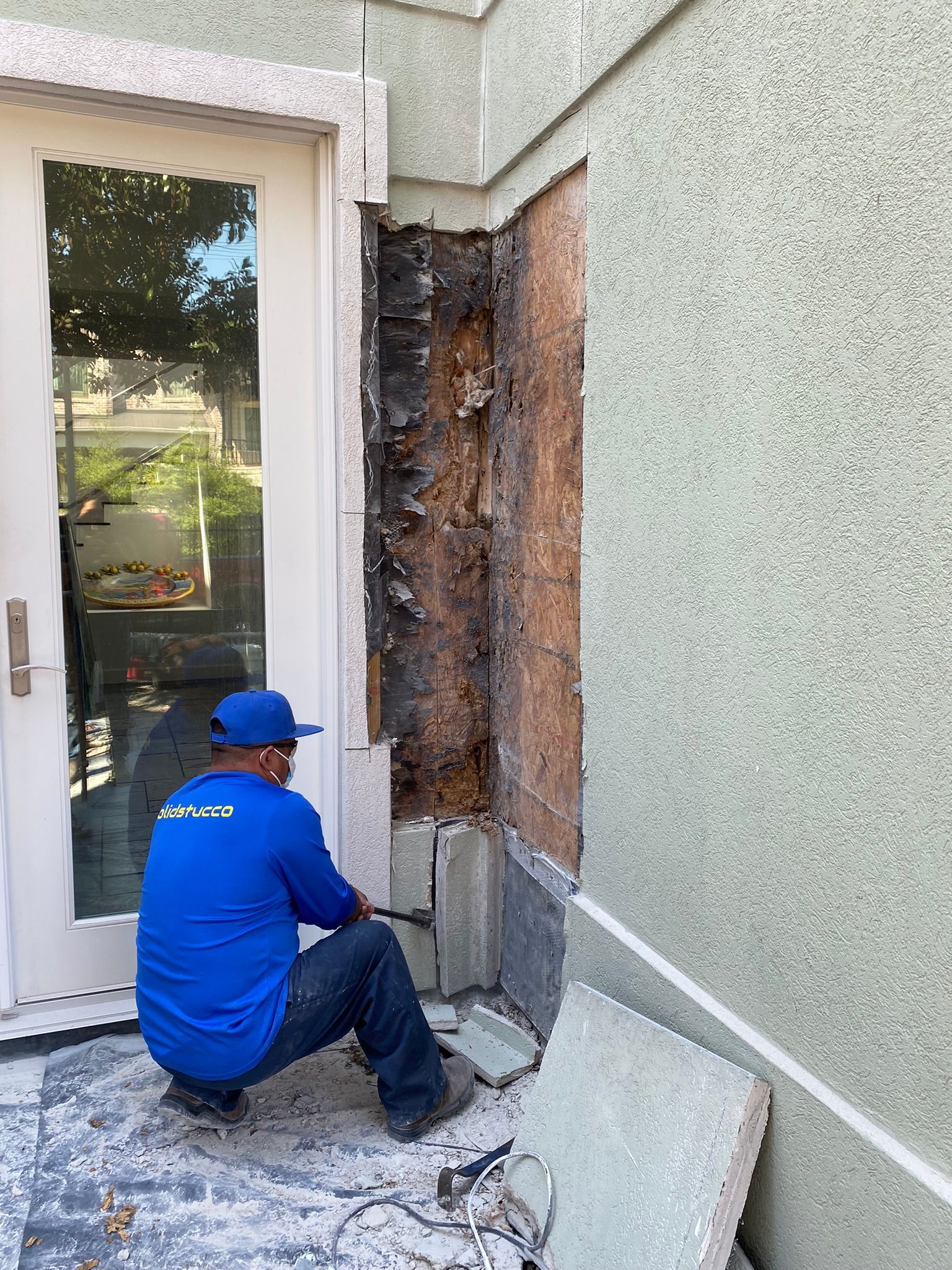 A man in a blue shirt is kneeling down in front of a door.