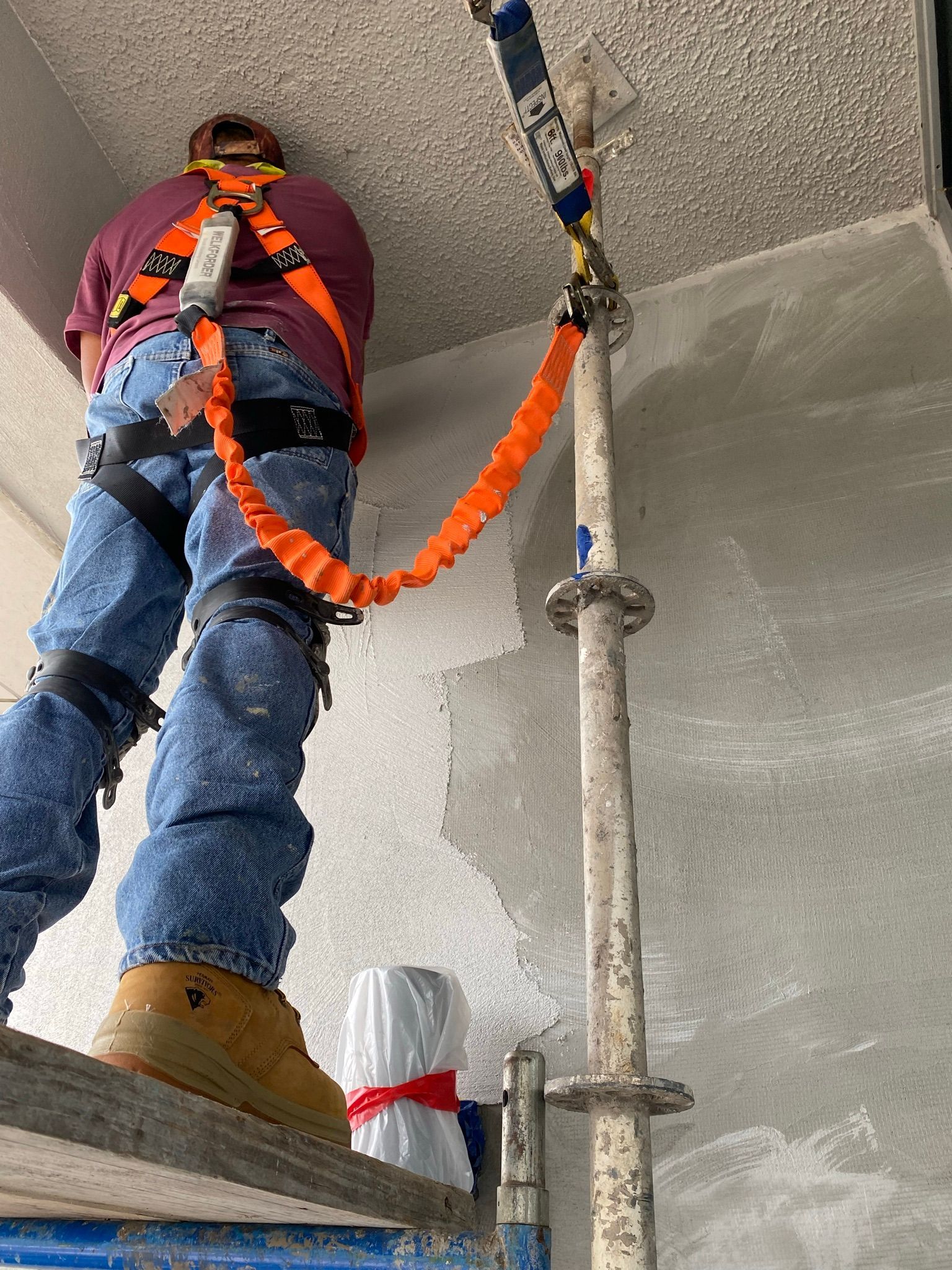A man wearing a safety harness is standing on a scaffolding.