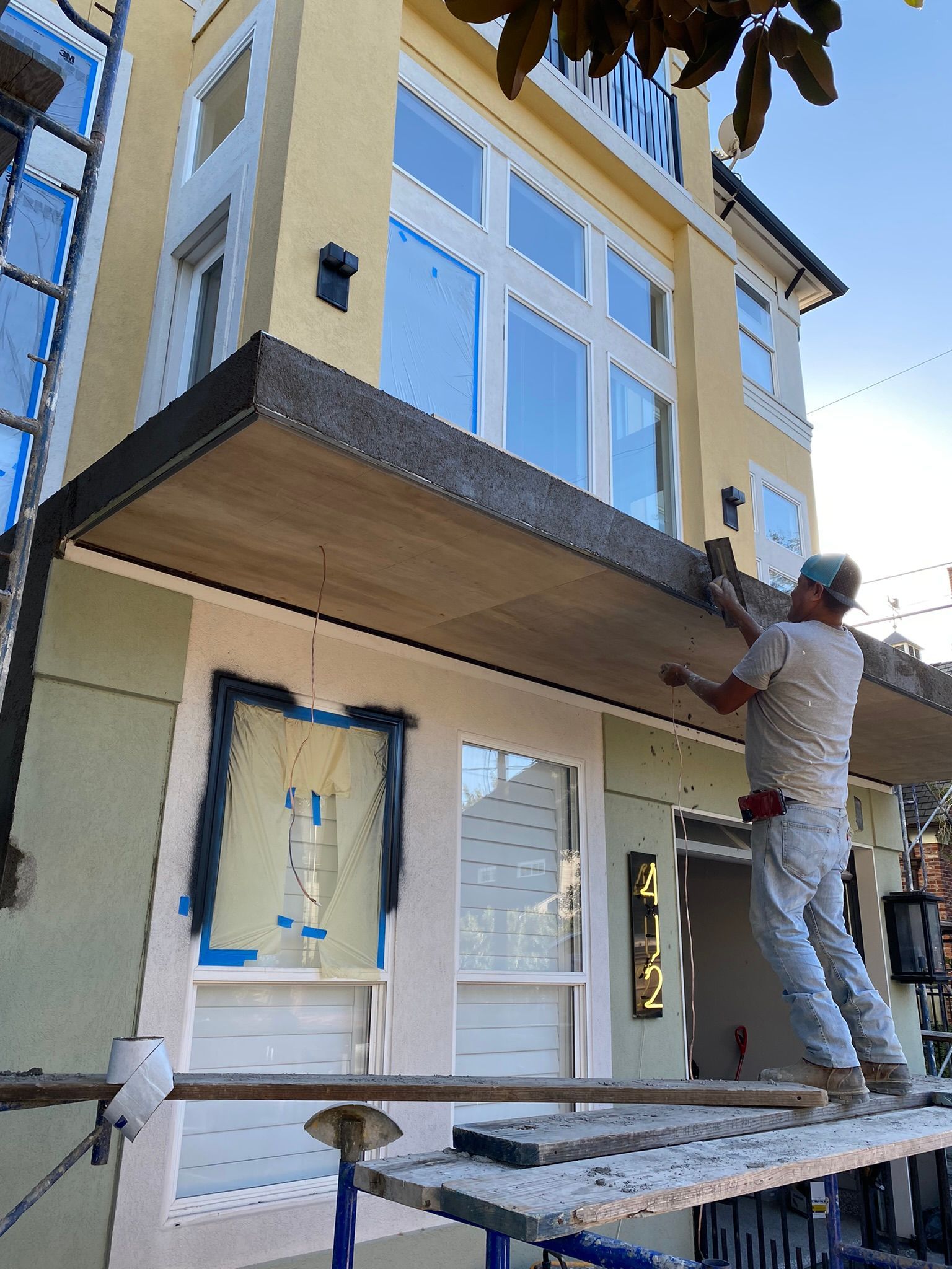 A man is standing on a scaffolding painting the side of a building.