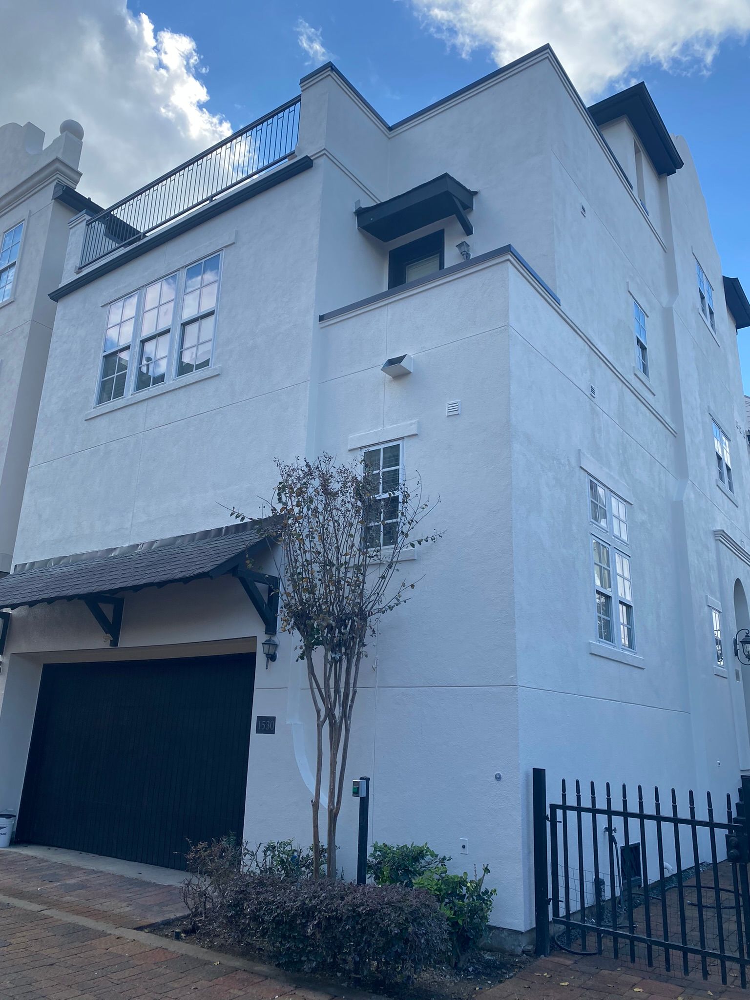 A white house with a black garage door and a fence in front of it.