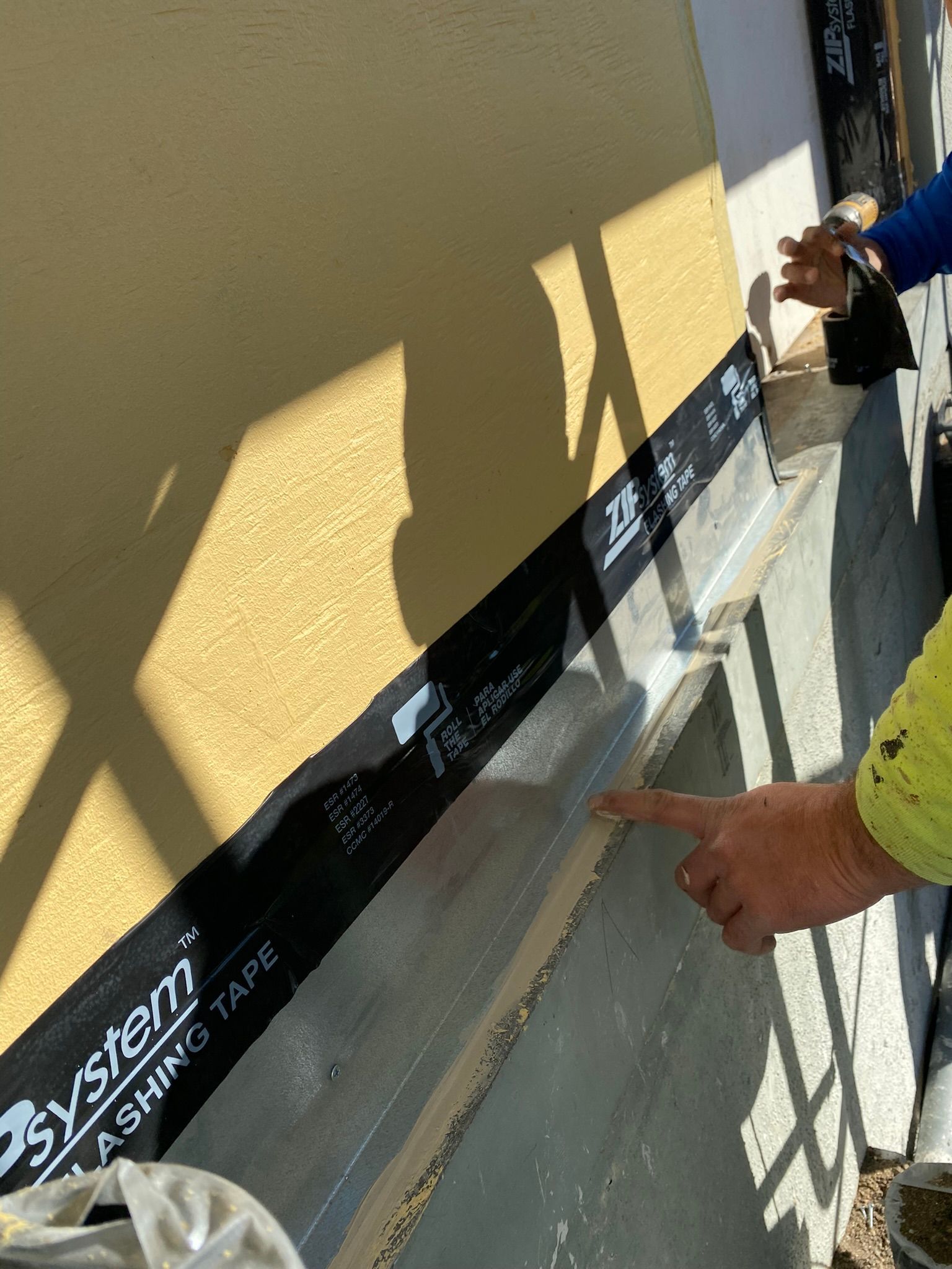 A person is pointing at a piece of tape on the side of a building.