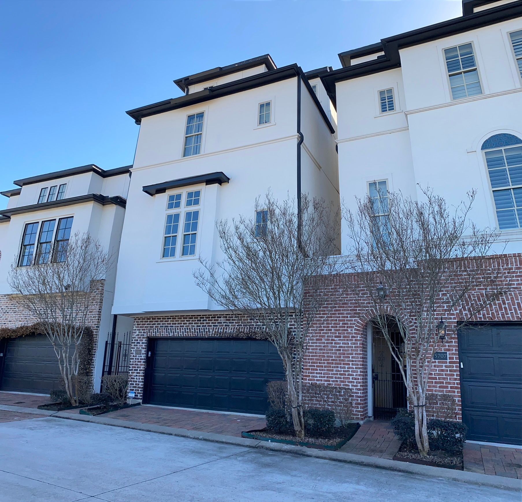 A white building with a brick wall and black garage doors