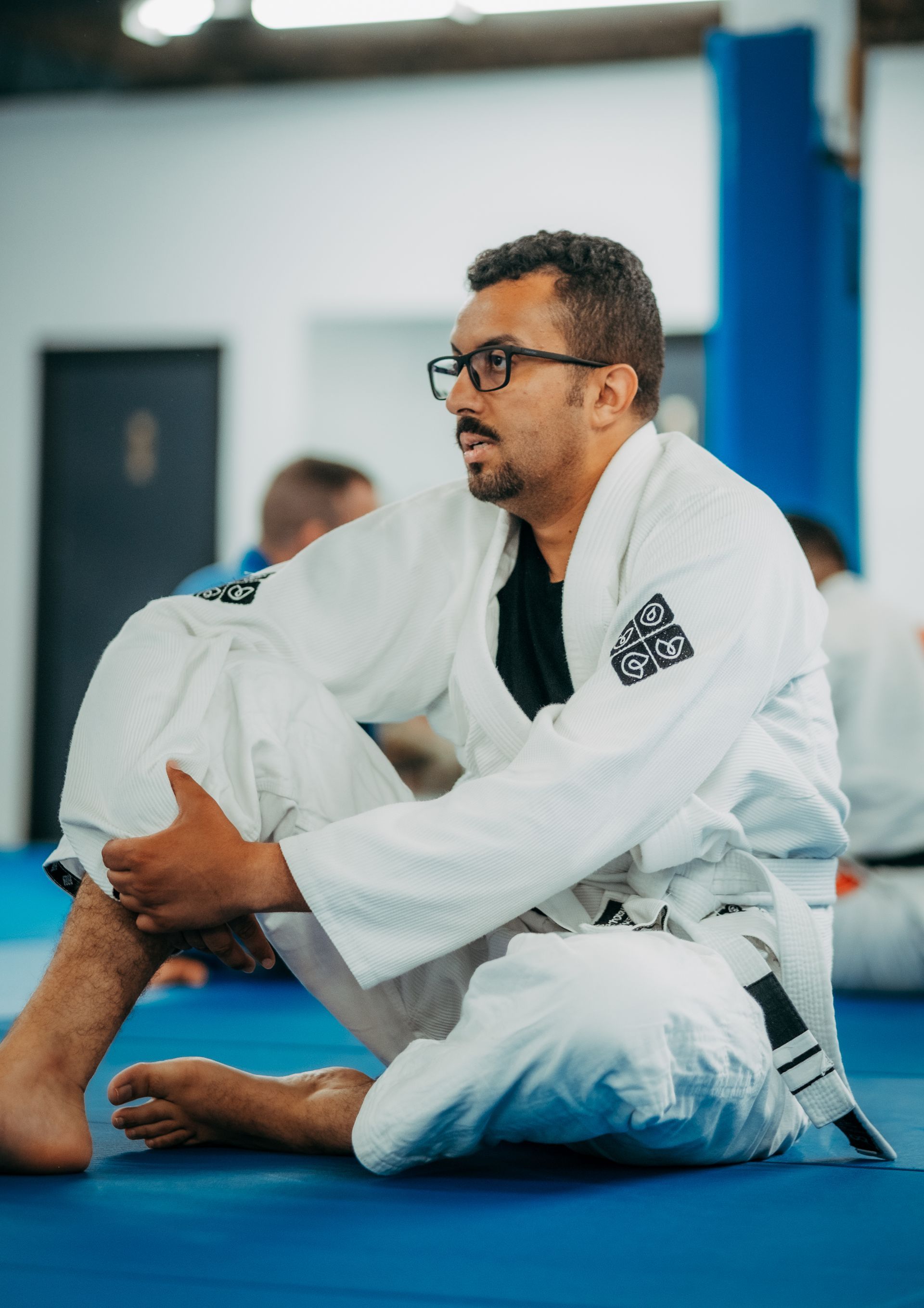 Man in white gi sitting cross-legged on blue mats in the best martial arts center in Ottawa, ON