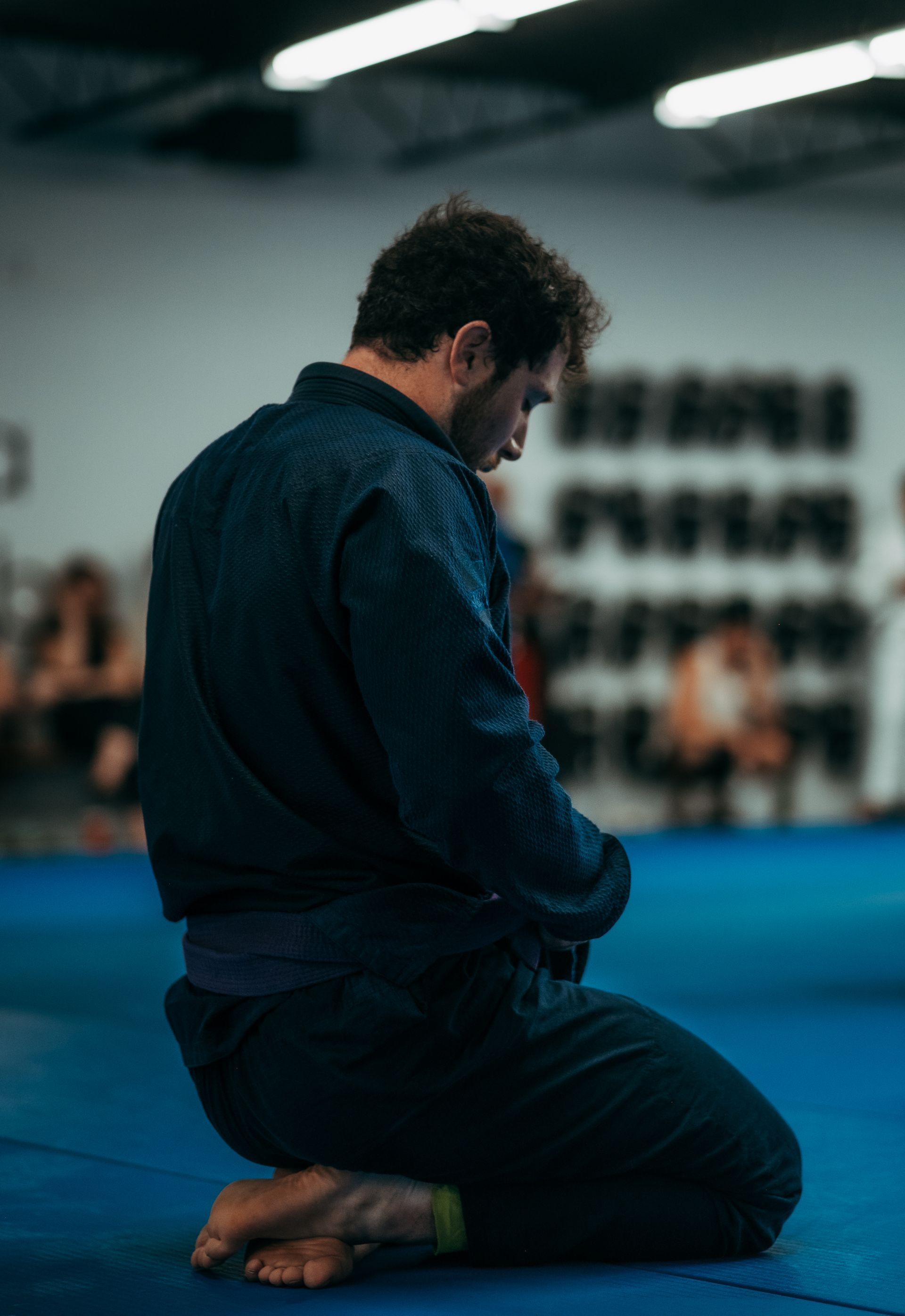 Person kneeling on a blue mat in the best martial arts center in Ottawa, ON, head bowed in a quiet pose