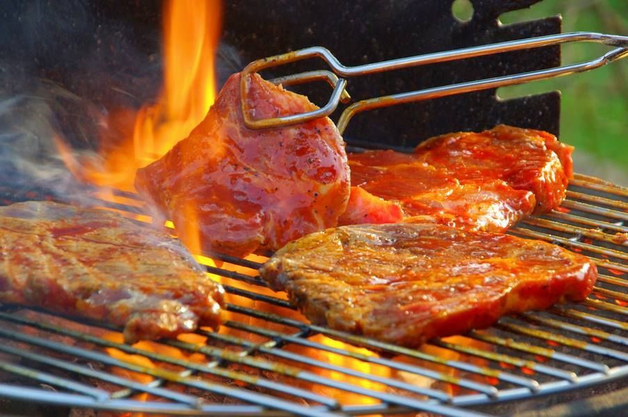 Steaks are cooking on a grill with flames behind them