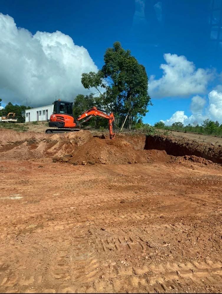 An Orange Excavator is Digging a Hole in a Dirt Field — Blue Gum Earthworks in Mareeba, QLD
