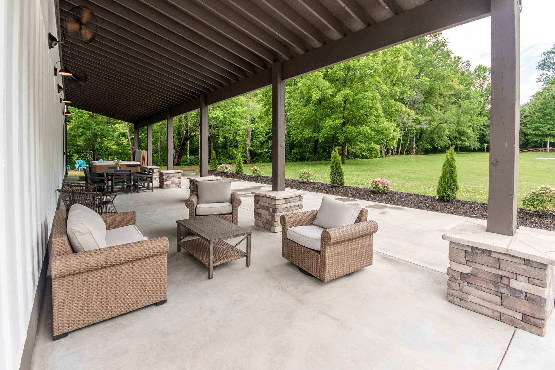Covered outdoor patio with wicker seating, dining table, and green lawn beyond
