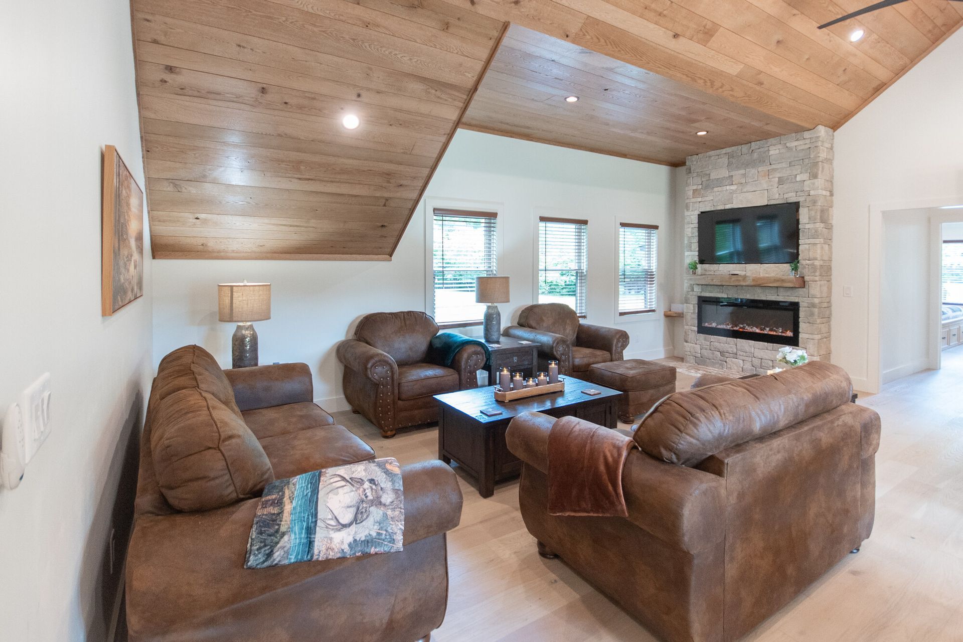 Bright living room with leather sofas, stone fireplace, TV, and vaulted wood ceiling