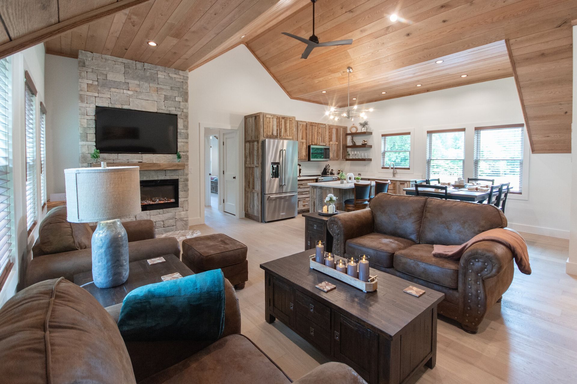 Spacious living room with stone fireplace, wood ceiling, leather sofas, and large windows overlooking a bright interior.