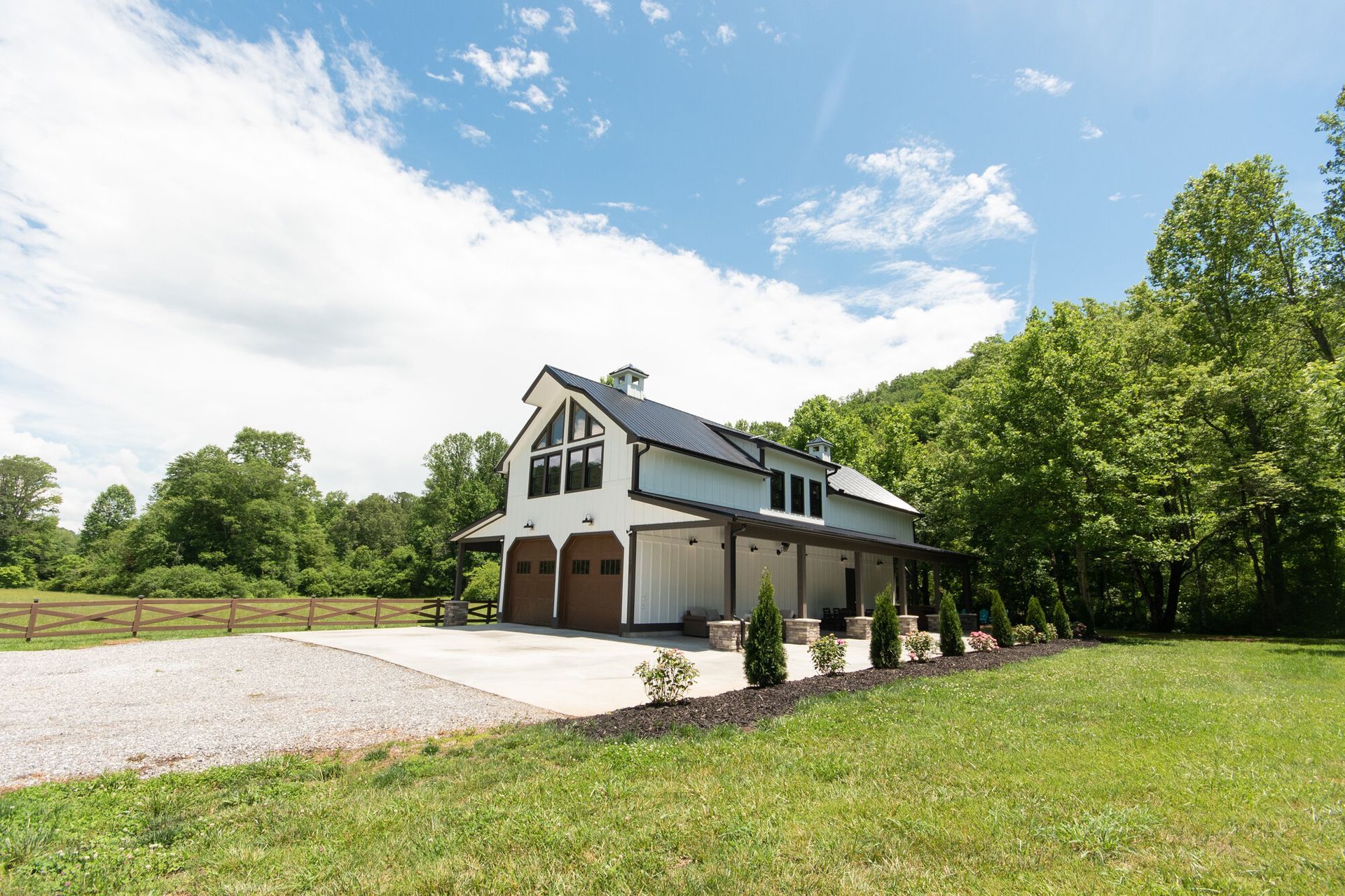 White two-story house with a three-car garage, gravel driveway, and trees on a sunny day