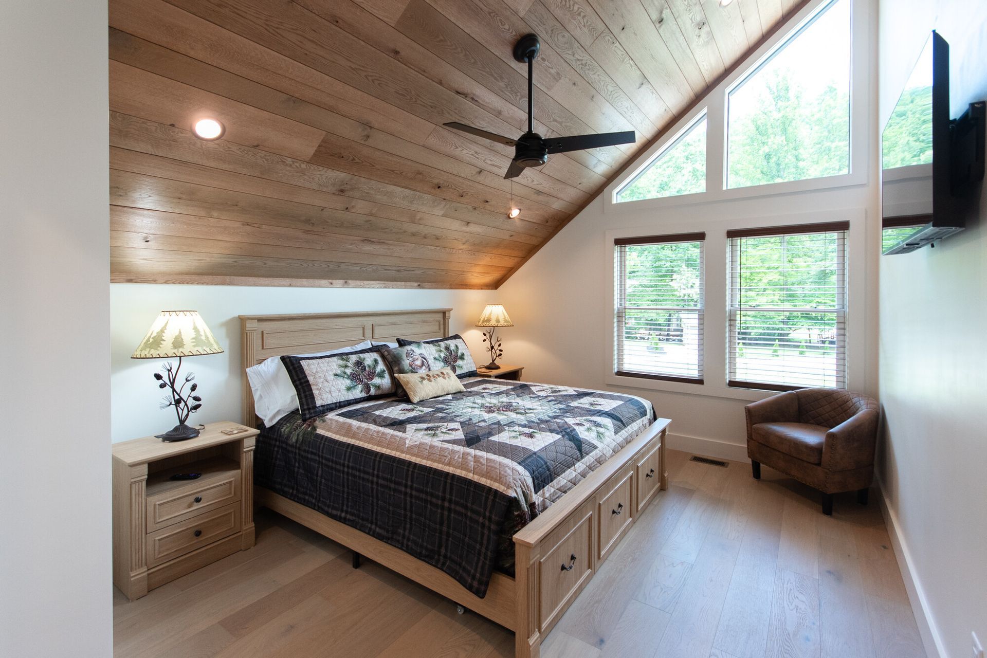 Cozy attic bedroom with wood ceiling, large windows, a bed, bedside lamps, and a ceiling fan