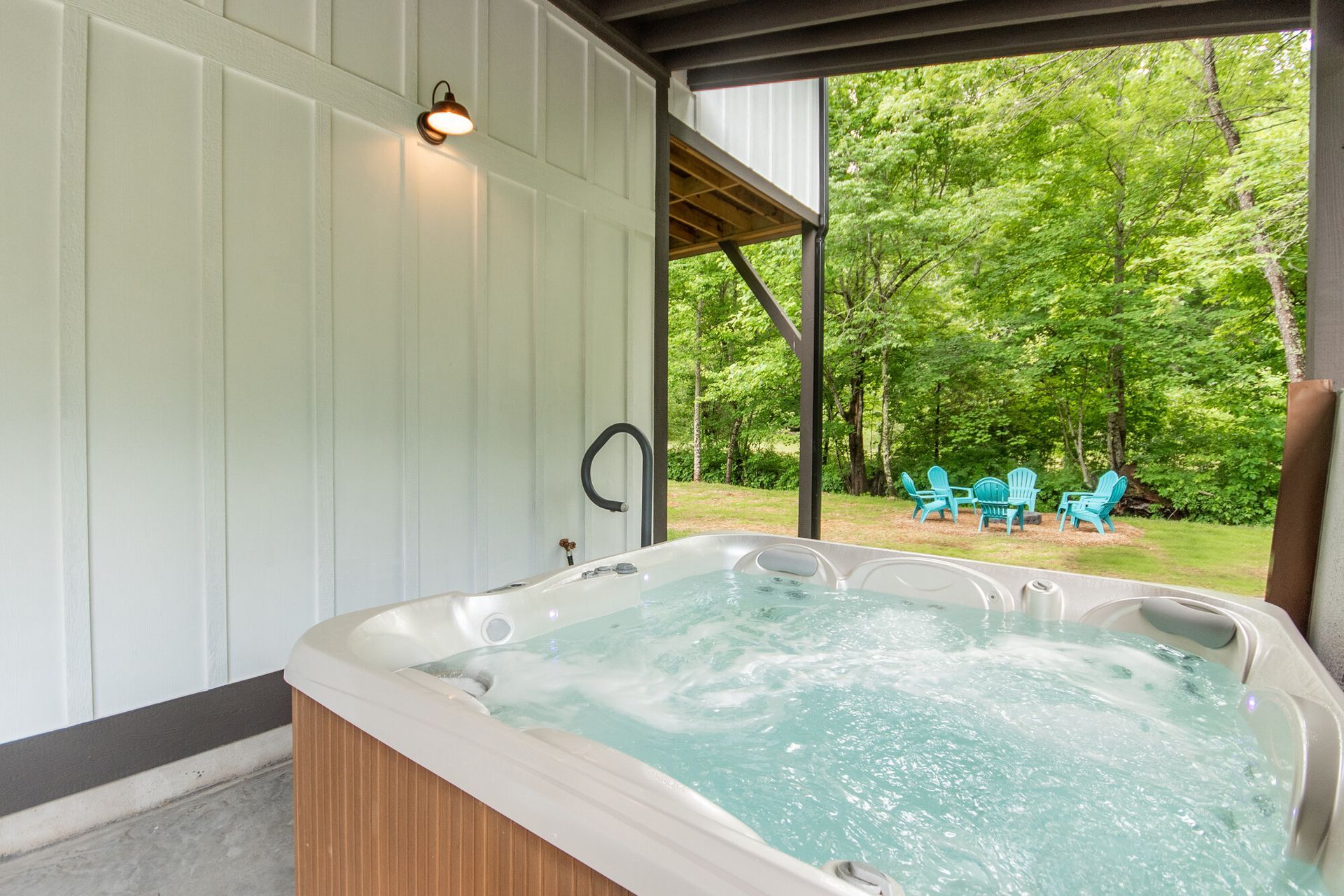 Covered hot tub on a patio overlooking a green backyard with blue lounge chairs