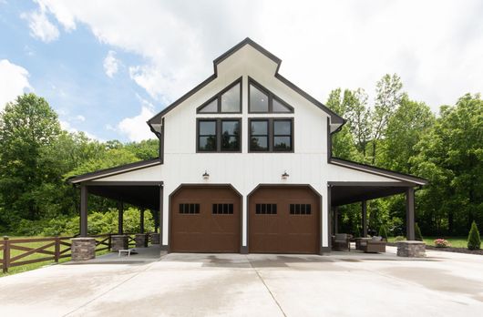 White two-bay garage with covered side porches and large windows in a wooded setting