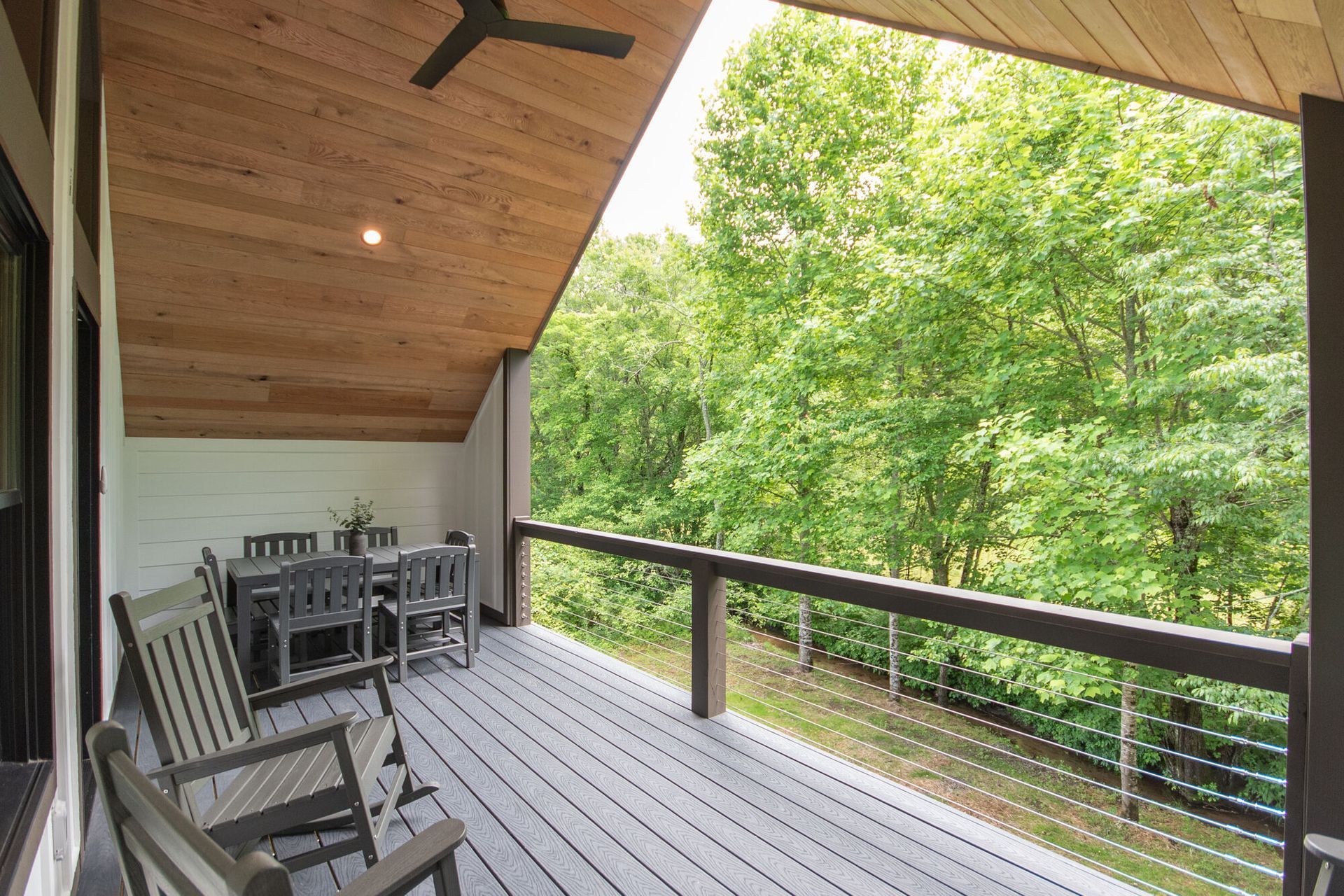 Covered wooden porch with rocking chairs overlooking a green forest and railing.