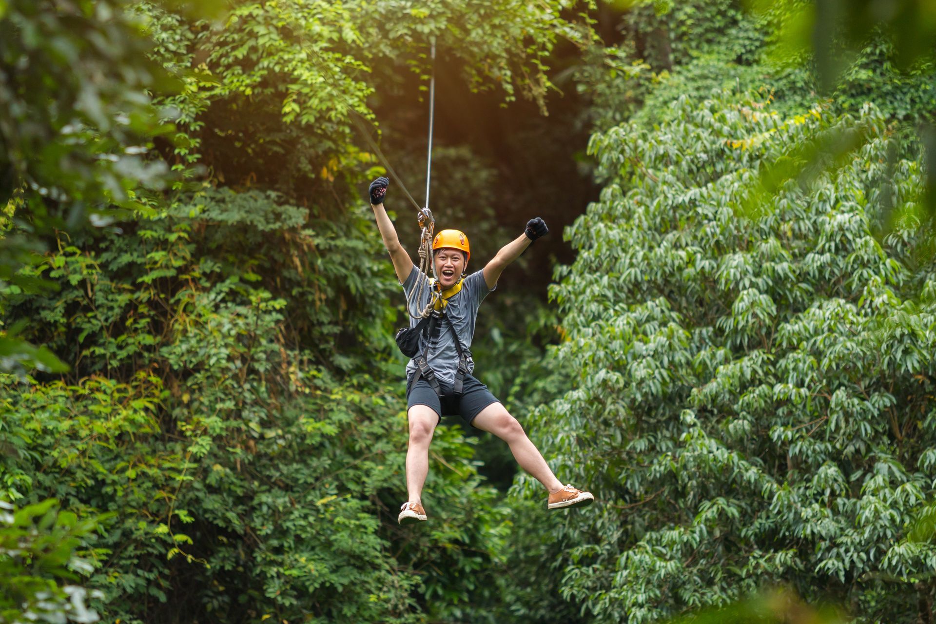 A woman is flying through the air on a zip line in the jungle.