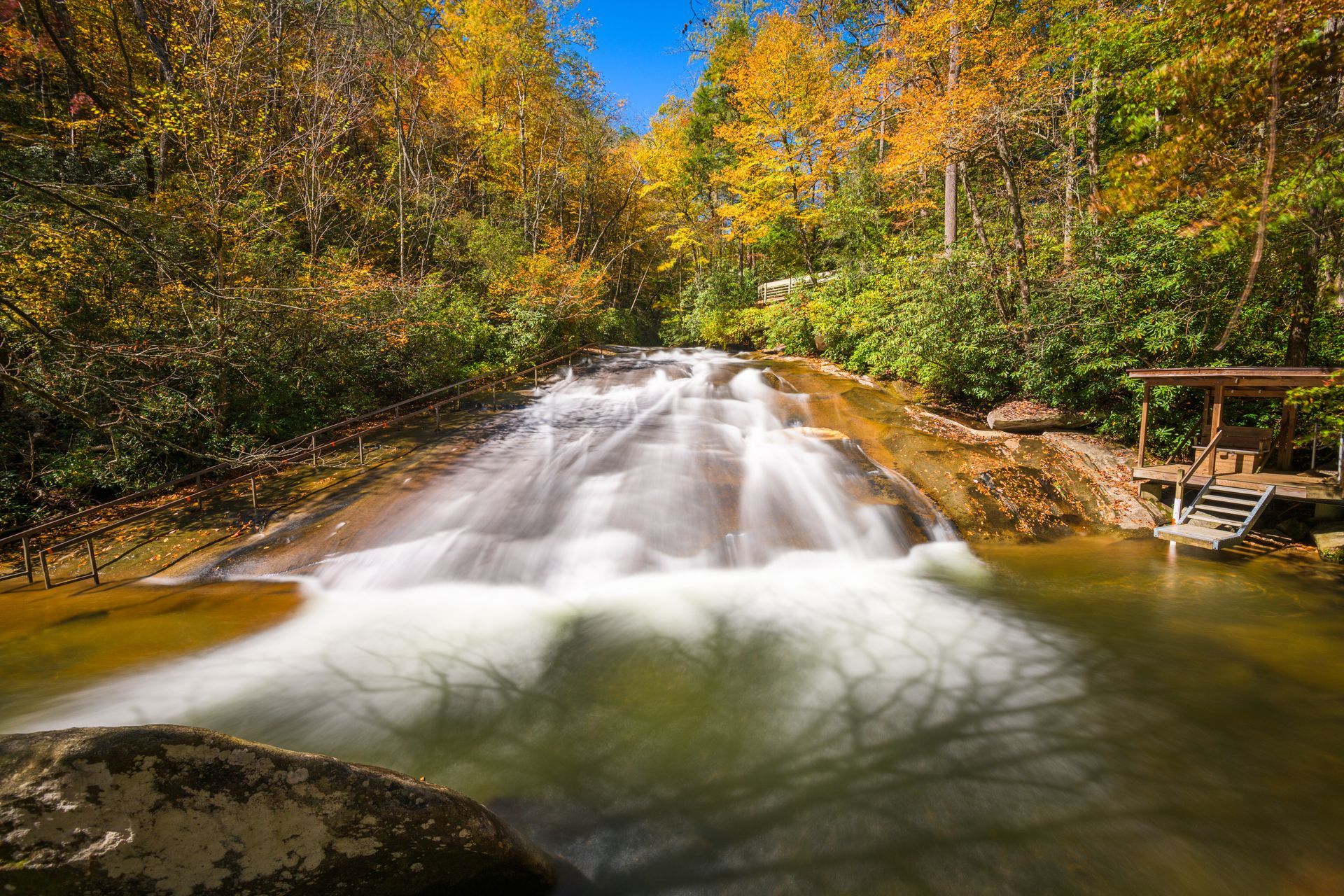 A waterfall is surrounded by trees and rocks in the middle of a forest and photo displays Sliding Rock Falls in NC