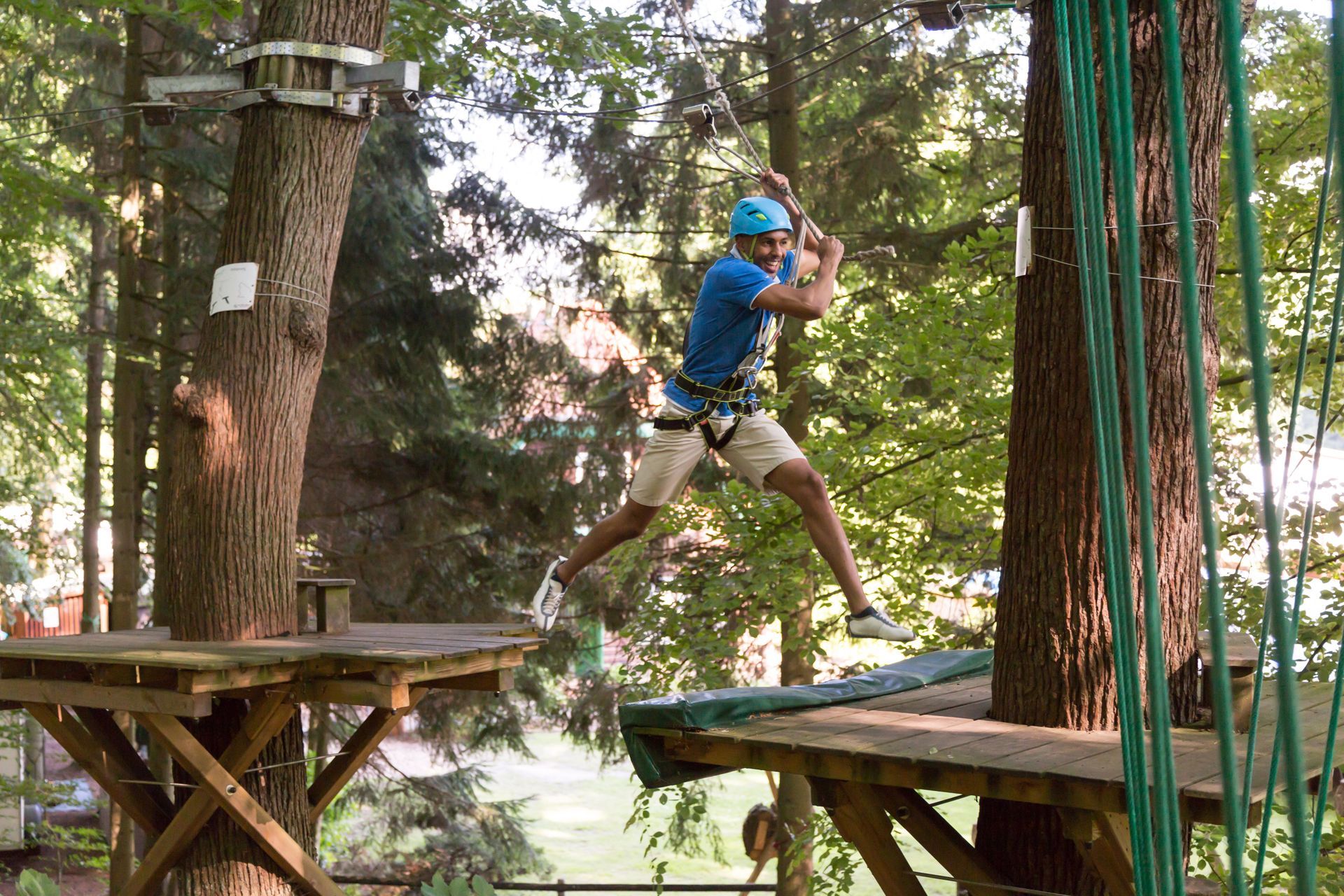 A man in a blue shirt is jumping between two trees
