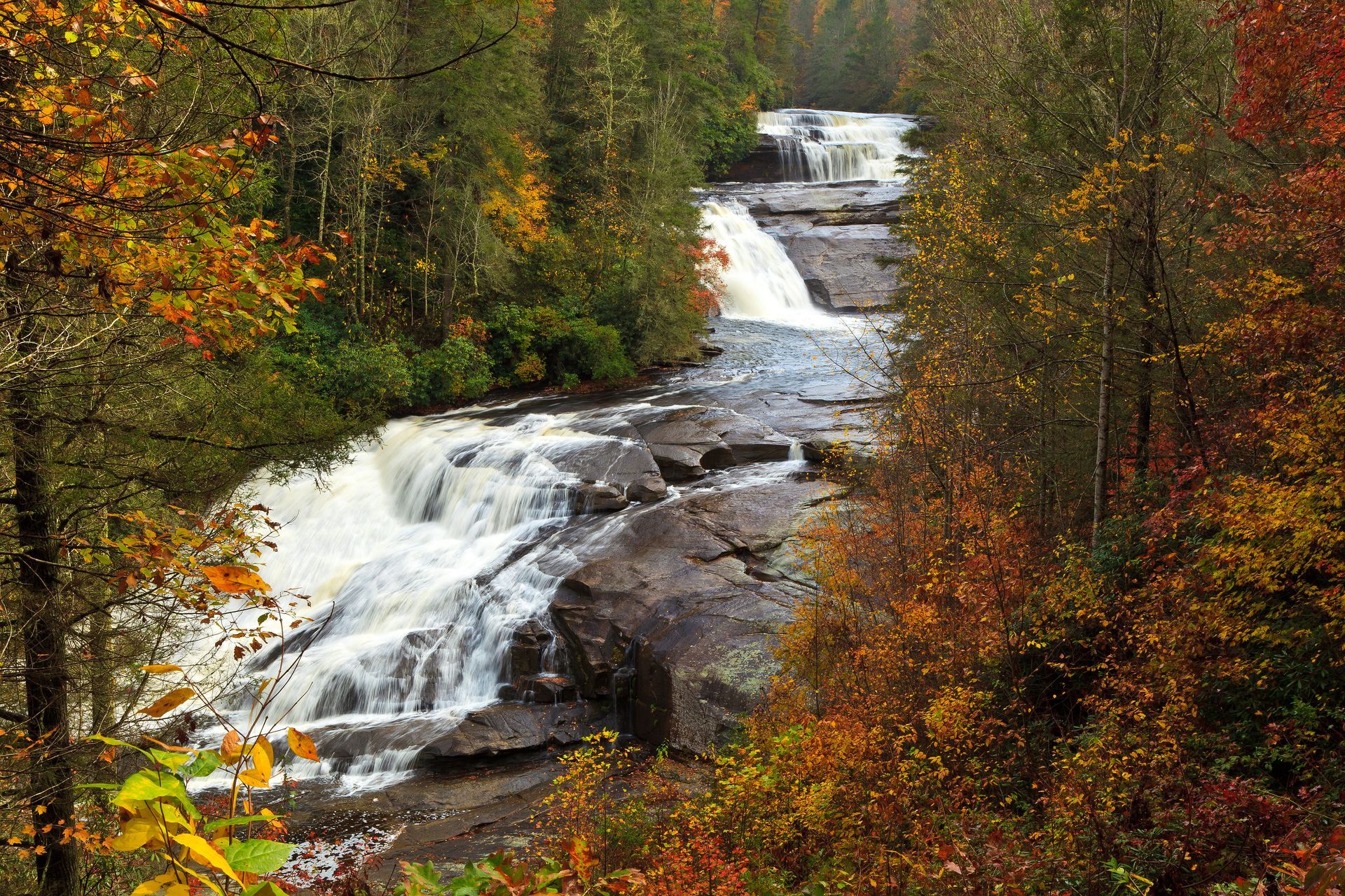 A waterfall is surrounded by trees in the middle of a forest and displays Triple Falls in NC