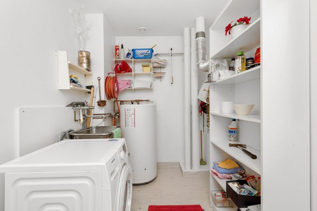 Narrow laundry room with a washing machine, water heater, and shelves of cleaning supplies