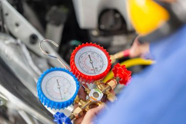 Mechanic using red and blue manifold gauges to service an air-conditioning system