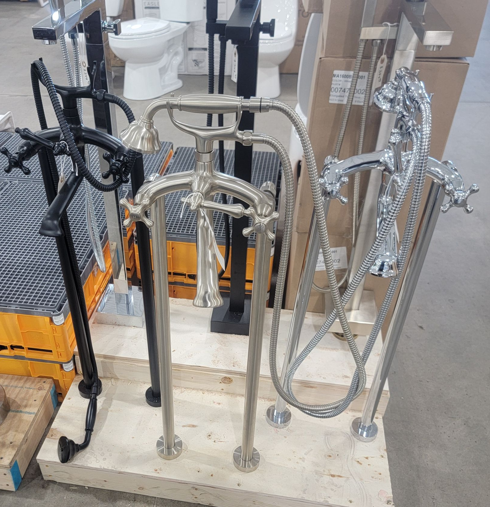 Assorted chrome and black metal railing/handrail posts displayed on a pallet in a warehouse