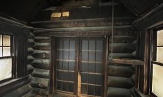 Intérieur d'une cabane rustique, avec murs en bois, fenêtres et portes doubles.