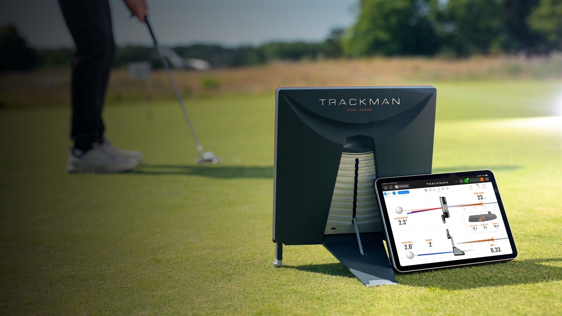Golfer using a putting aid with a tablet showing swing analysis on a green. The aid is black.