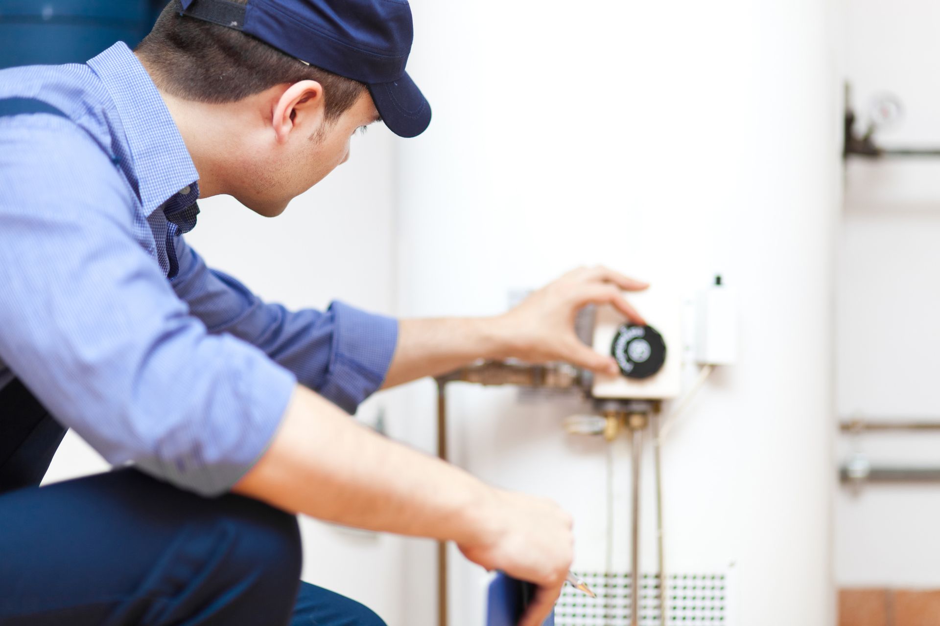 A man is kneeling down fixing a water heater.