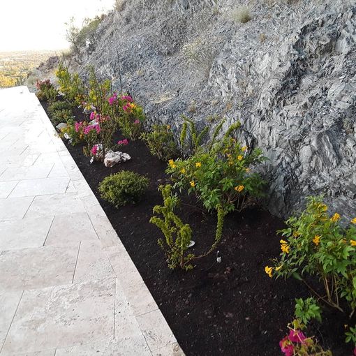 Stone walkway beside a rocky wall with a narrow flower bed of pink and yellow blooms