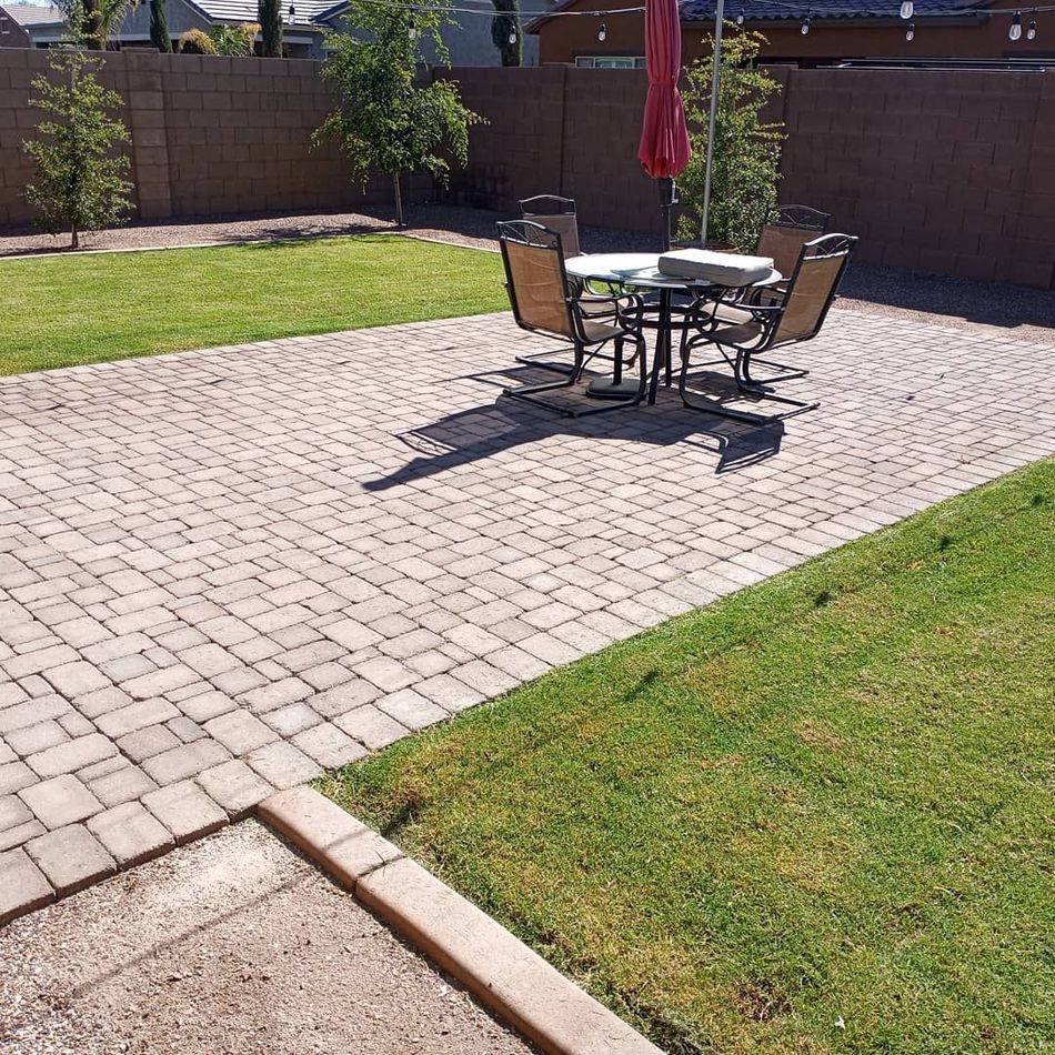Patio with a round outdoor dining table and chairs on a paver patio beside a grassy lawn.
