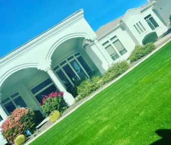 White mansion with arched porch and manicured green lawn under a bright blue sky