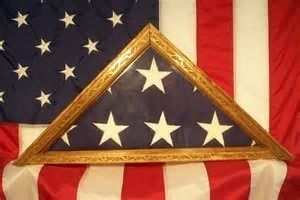 Folded American flag in a triangular display case, set against a full US flag backdrop.